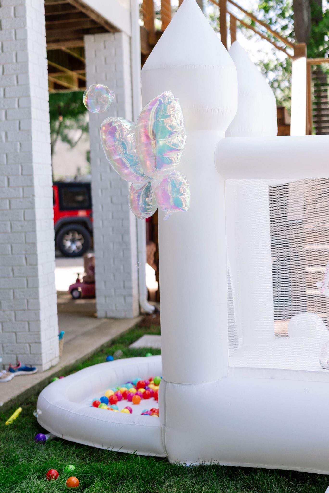 White inflatable bounce house with iridescent butterfly balloon and attached ball pit filled with colorful balls.