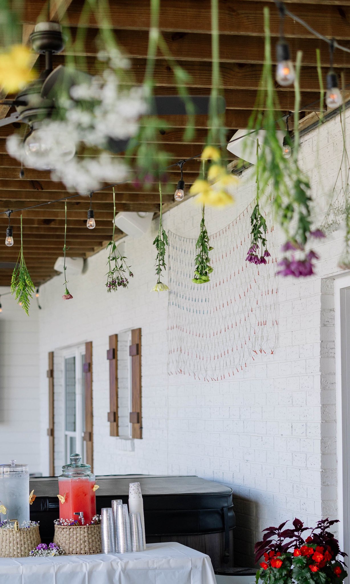 Outdoor patio decorated with hanging flowers and string lights above a serving bar with drinks.