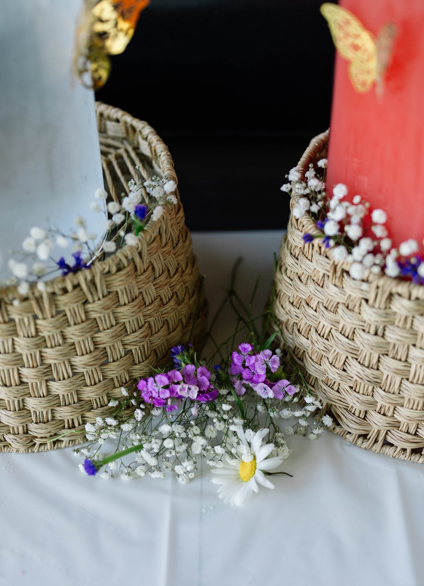 Two woven baskets containing candles decorated with gold butterflies, baby's breath, and a small daisy arrangement.