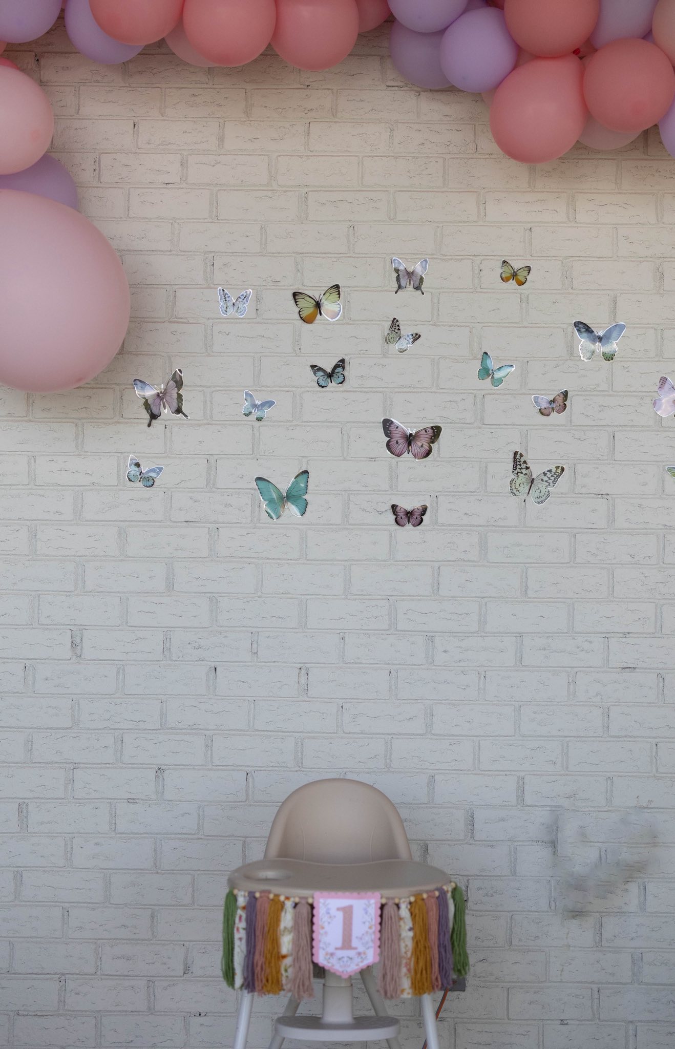 High chair for first birthday party decorated with butterfly theme wall balloons and decals