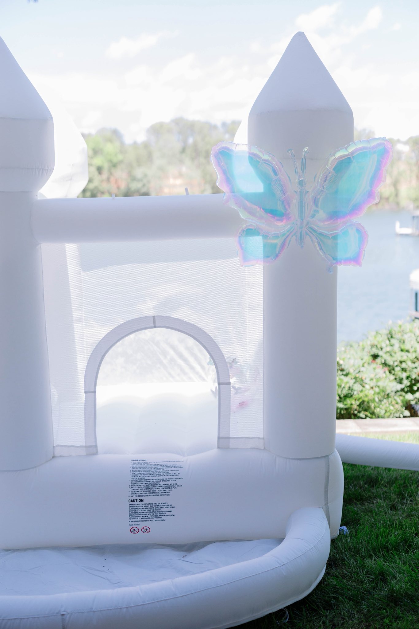 White inflatable bounce house with iridescent butterfly balloon attached to the pillar.