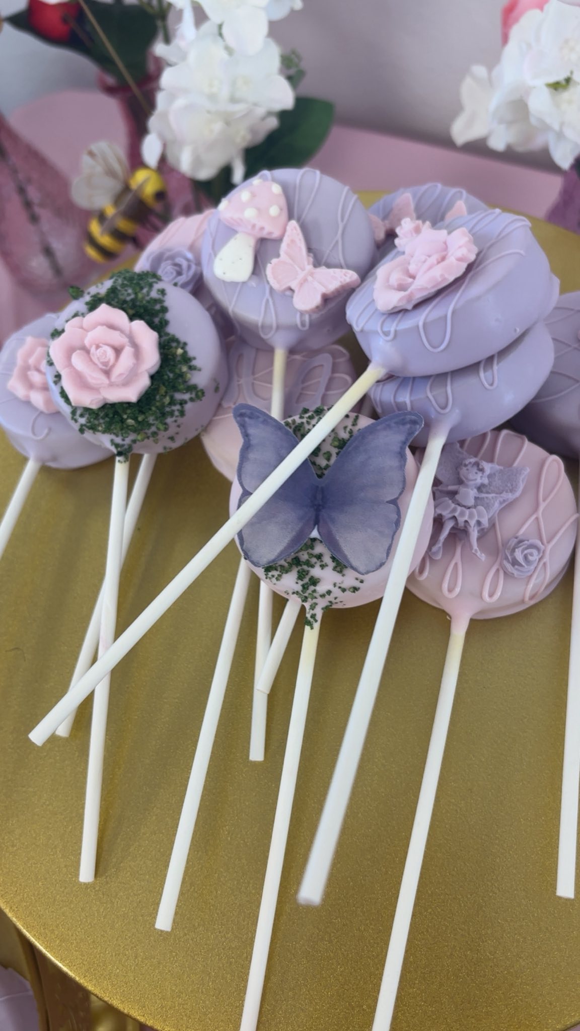Lavender-colored chocolate covered cookie pops decorated with pink roses, butterflies, and mushrooms.