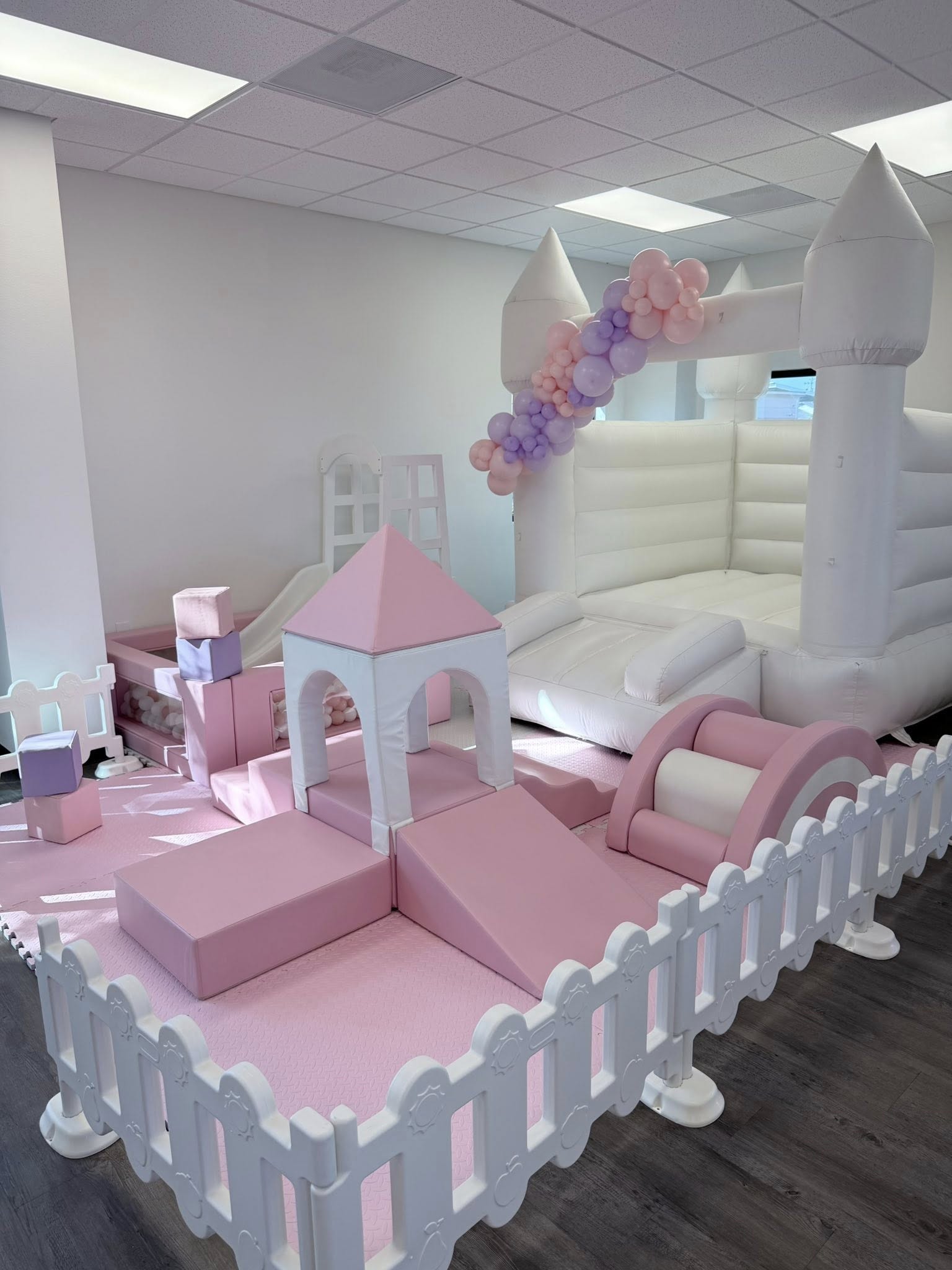 Soft play indoor party area with a white bouncy castle, pink foam climbing blocks, and a ball pit