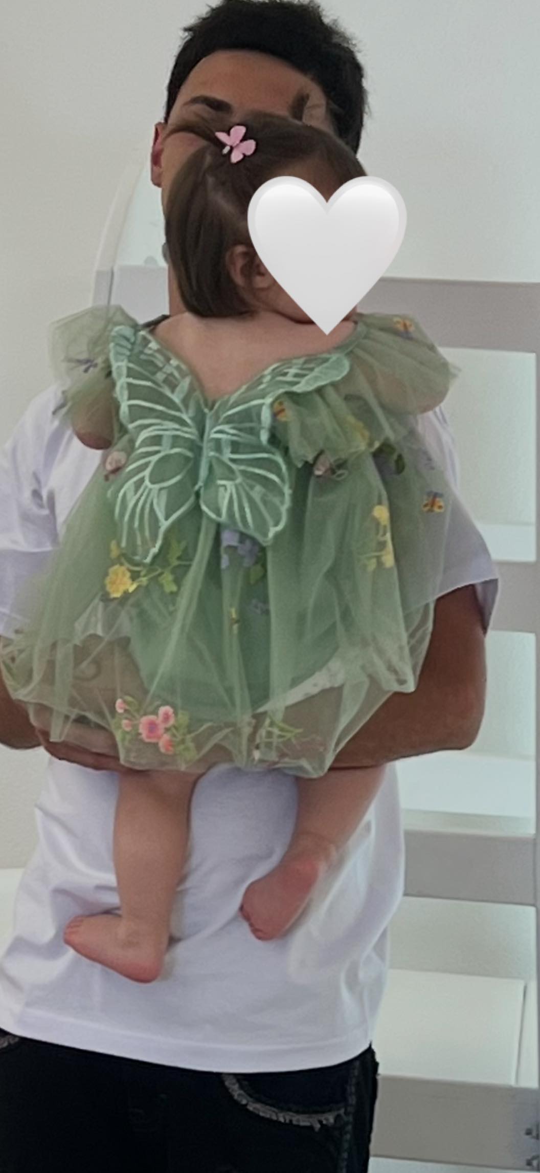 Toddler wearing a sage green backless tulle dress with floral embroidery and butterfly wing accents.