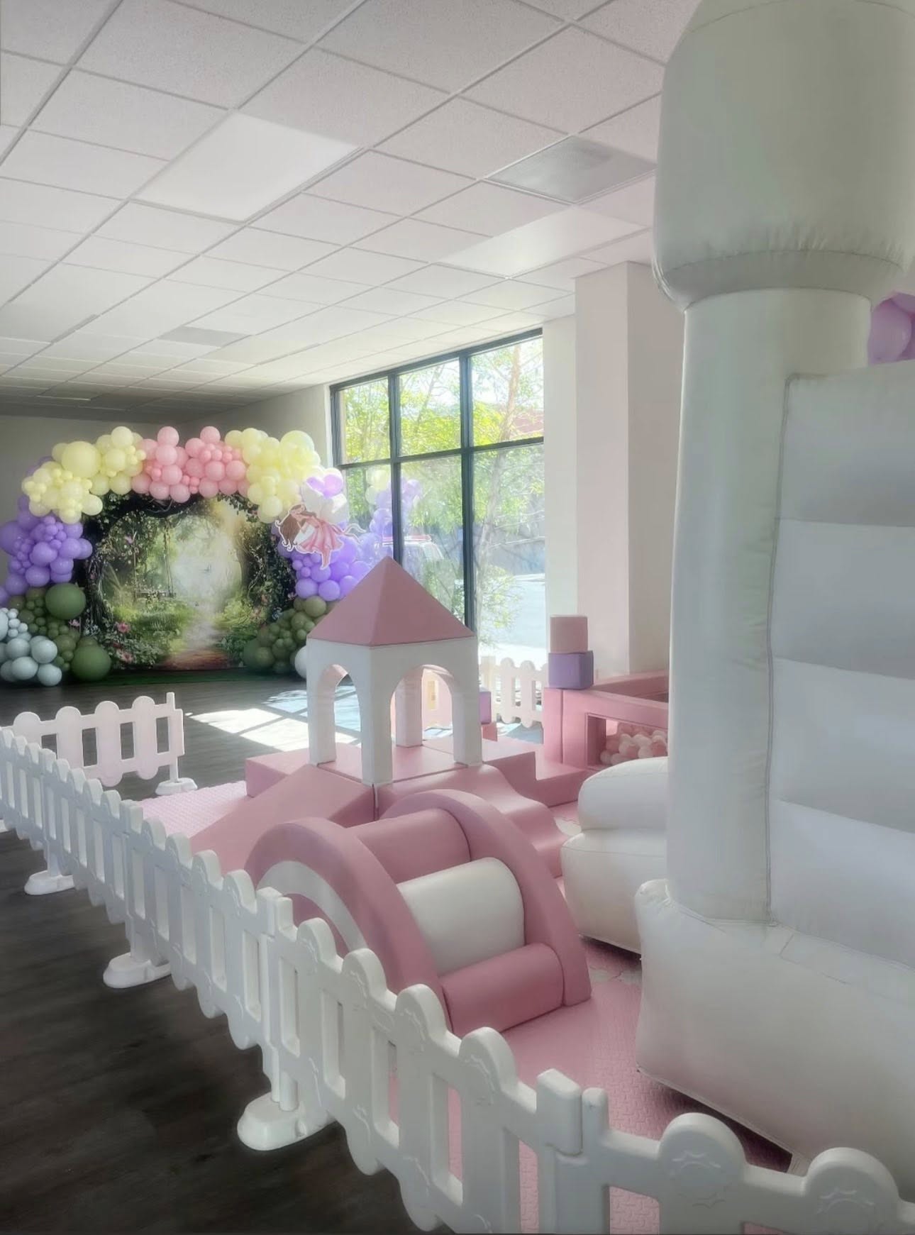 Soft play foam playground set in pink and white with a white inflatable bouncy castle and backdrop decoration