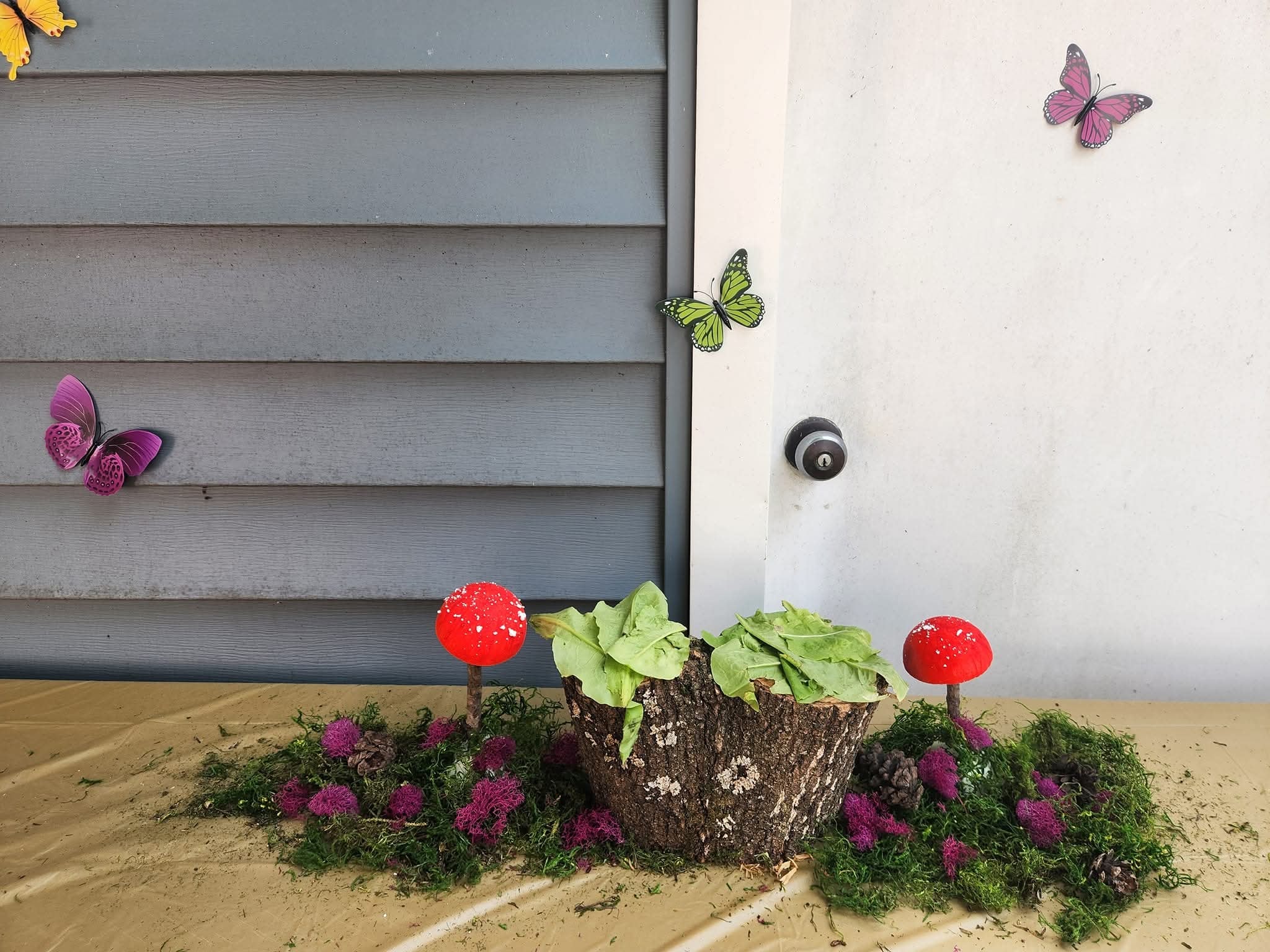 Tabletop fairy garden centerpiece with red mushrooms, moss, and leafy greens.