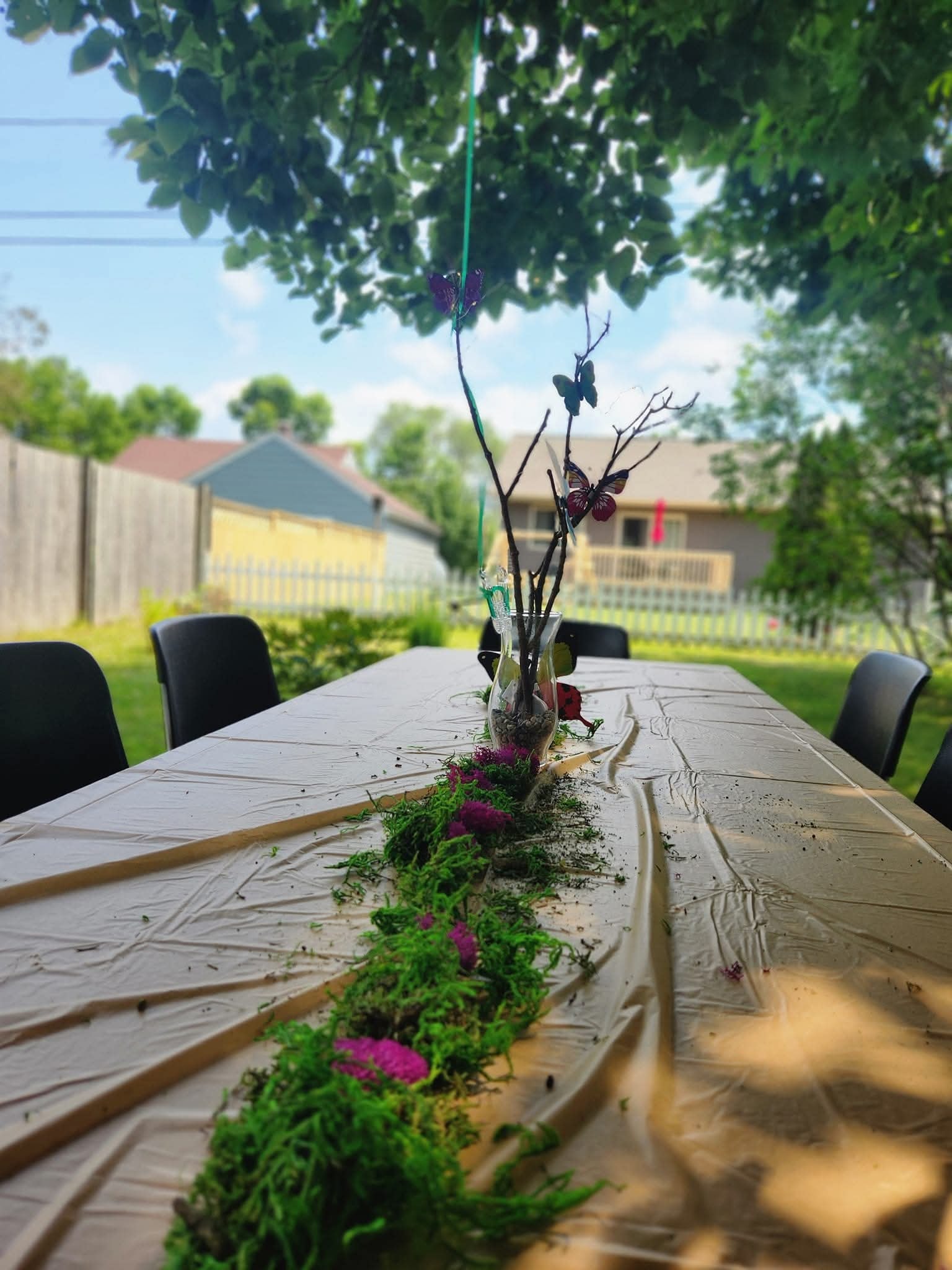 Outdoor dining table set with a moss runner and a decorative branch centerpiece with butterfly accents.