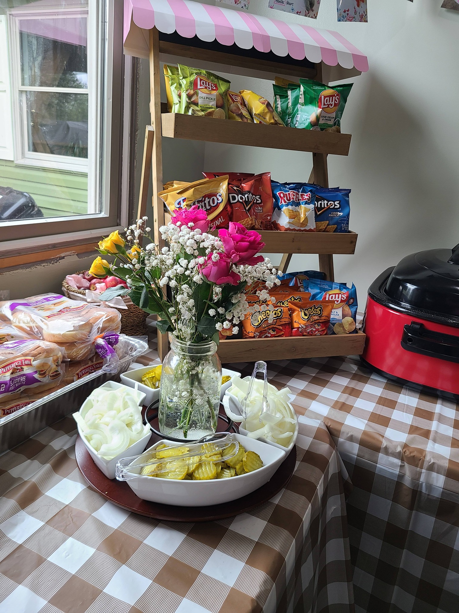 Snack bar display with a three-tiered shelf containing various chip bags, plus a serving tray of pickles and onions.