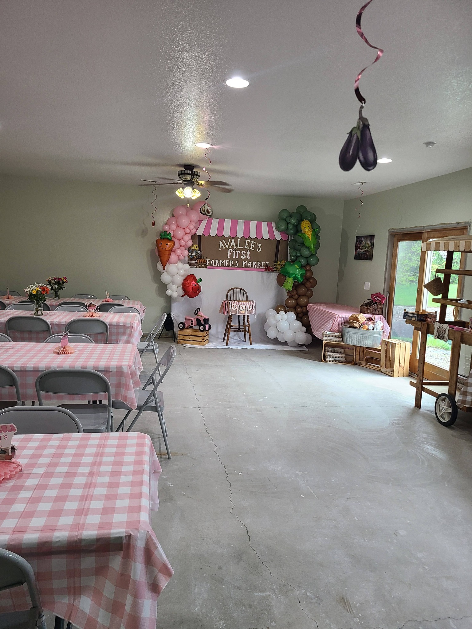 Events room decorated for a baby's farmer's market themed first birthday party with pink and white gingham tables.