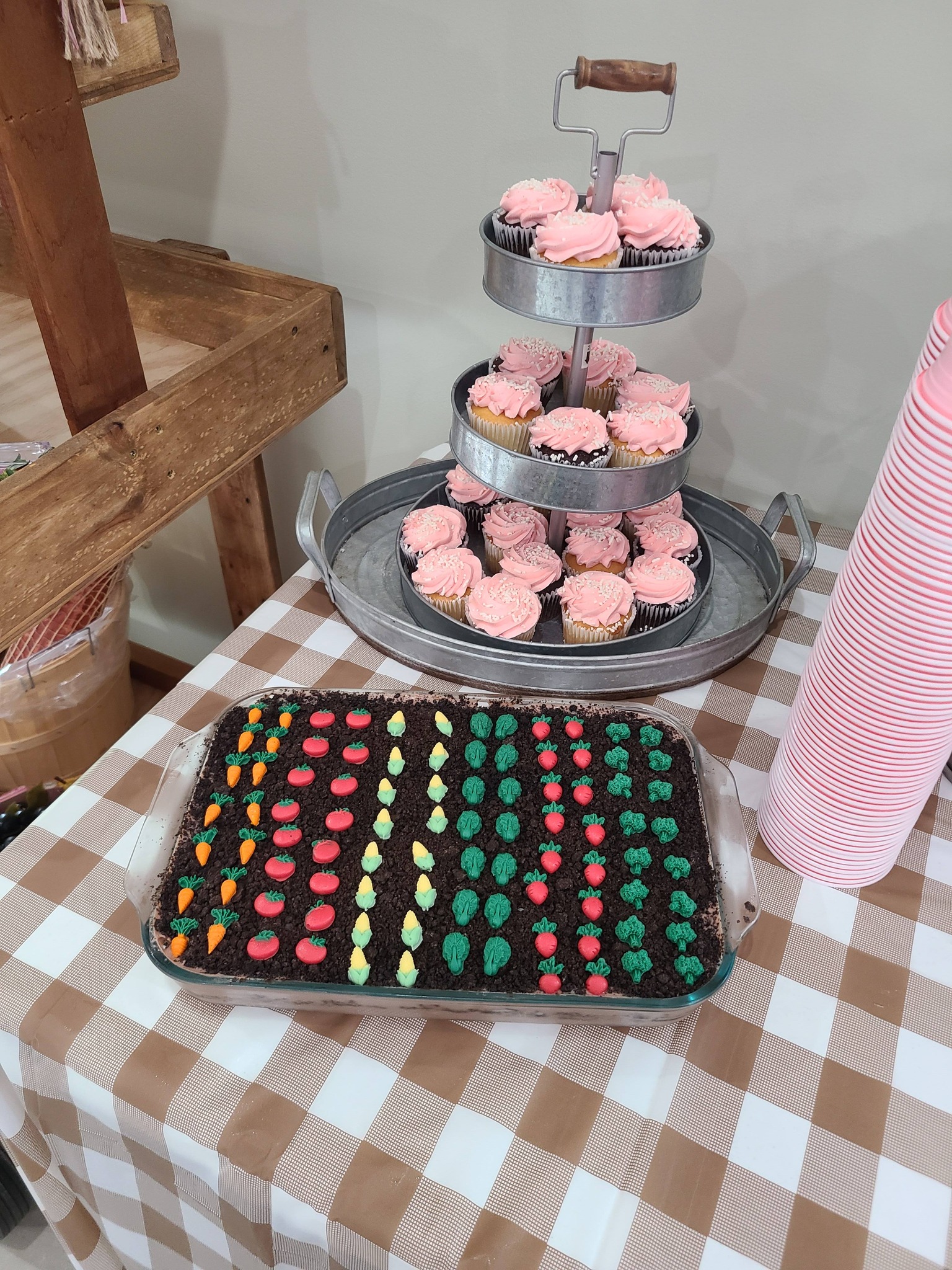 Garden-themed dessert table with a three-tier stand of pink cupcakes and a vegetable patch cake.