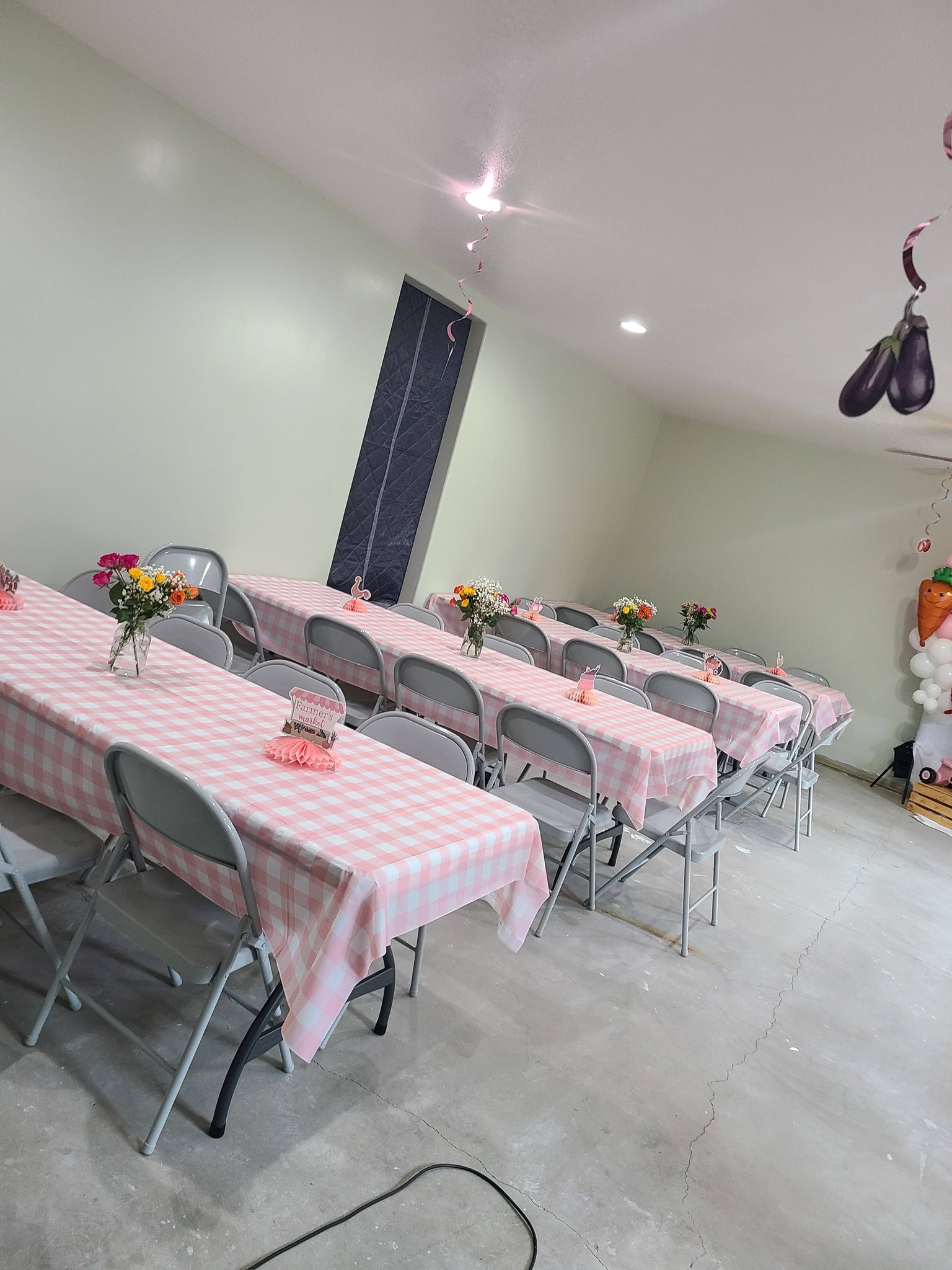 Event tables set up with pink gingham tablecloths, floral centerpieces, and Farmer's Market themed decorations.