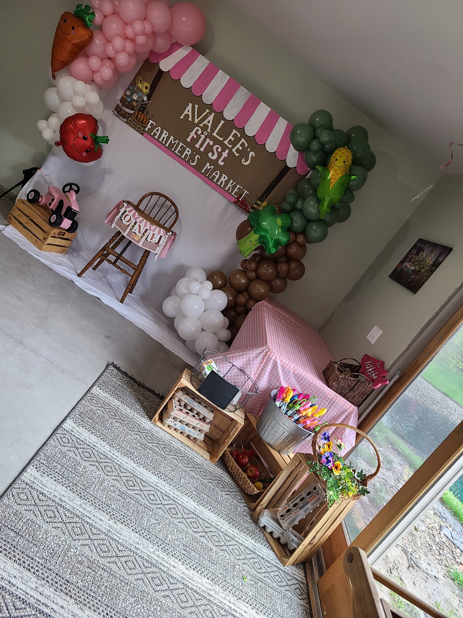 Farmer's market themed first birthday party decorations with balloons, a wooden high chair, and produce crates.