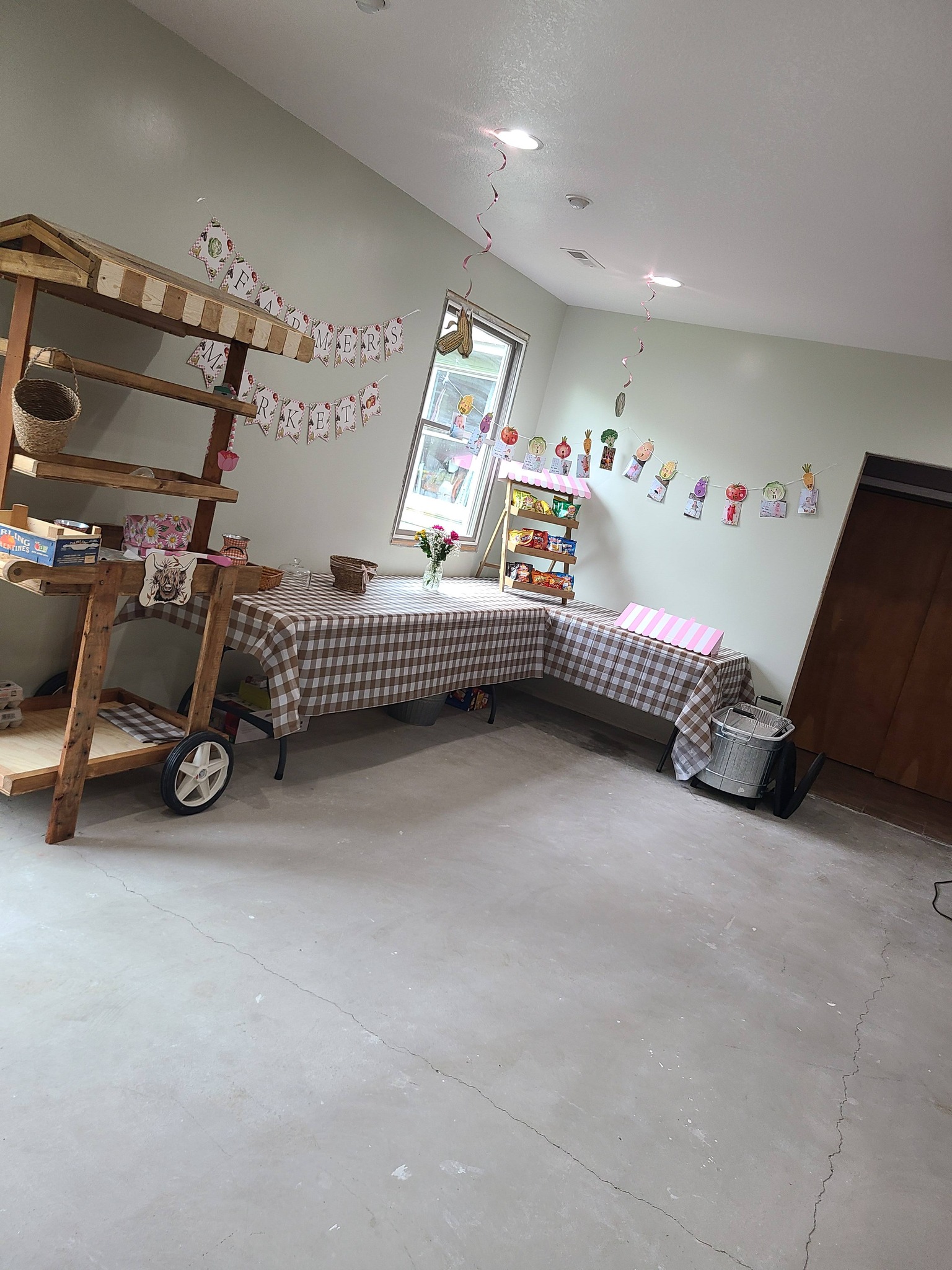 A Farmers Market themed party display featuring a wooden cart, gingham tablecloths, and veggie-themed decorations.