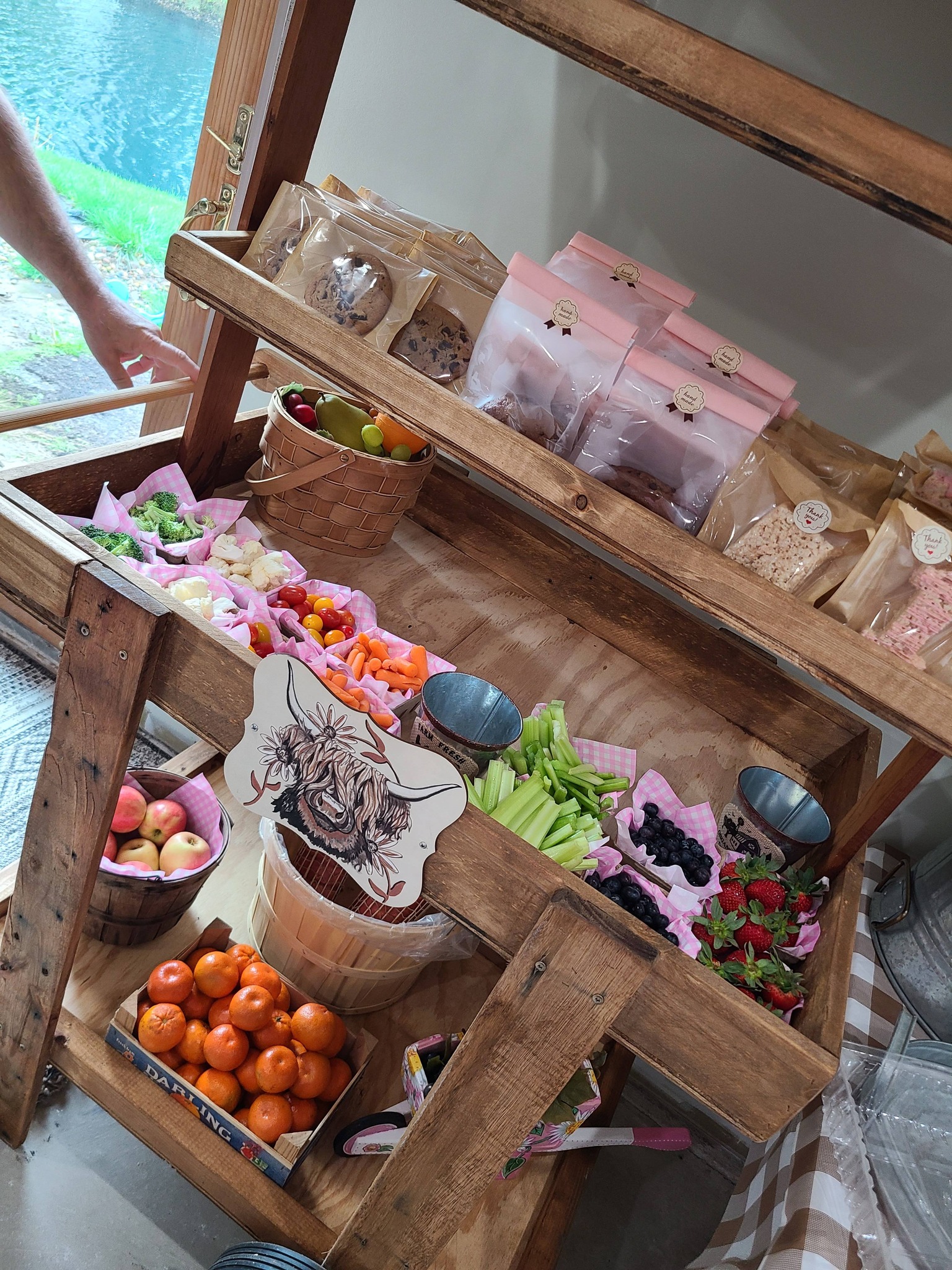 Wooden tiered produce stand filled with fresh fruit, vegetables, and packaged handmade snacks