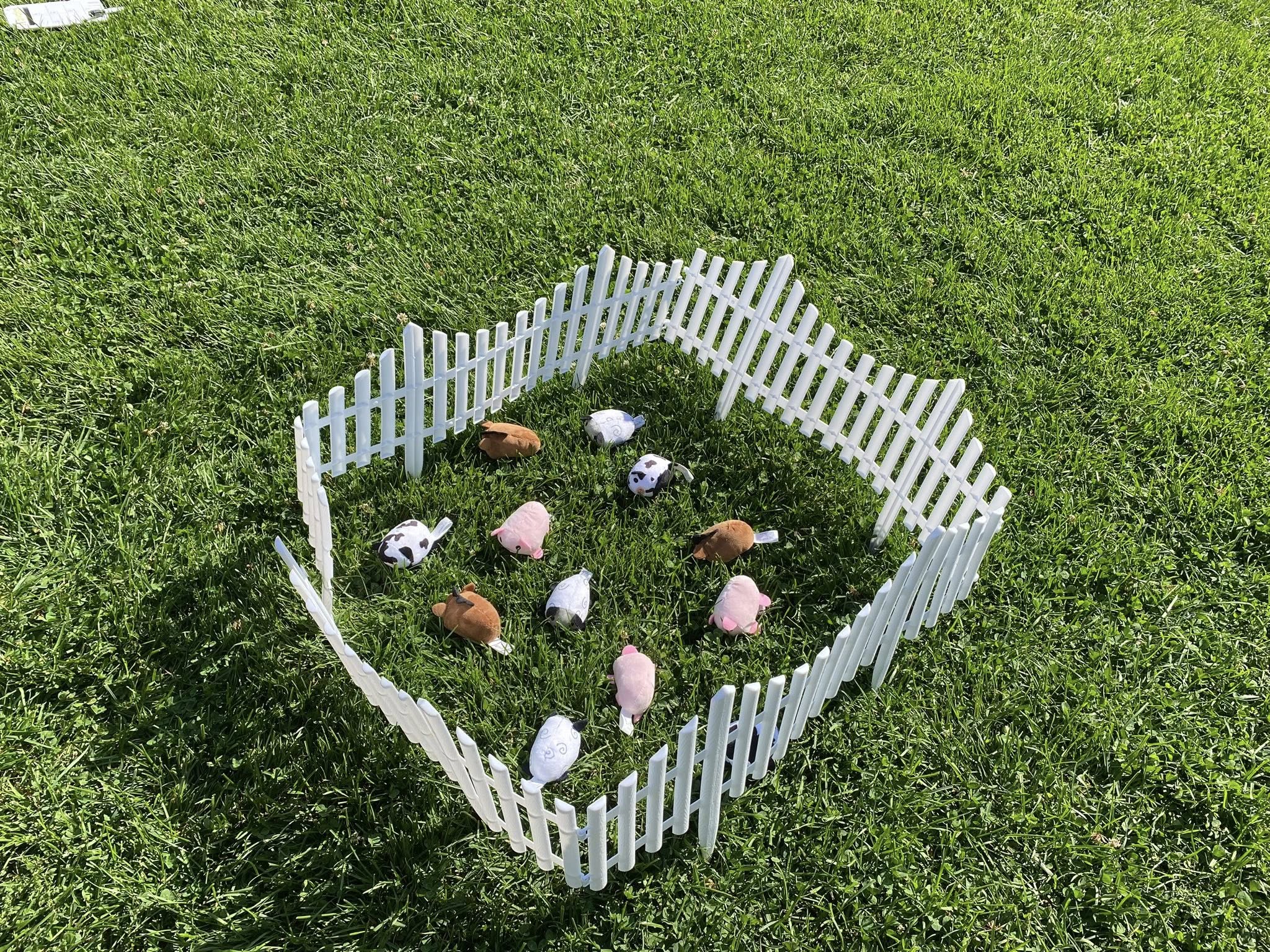 Small plush farm animals inside a white picket fence on green grass
