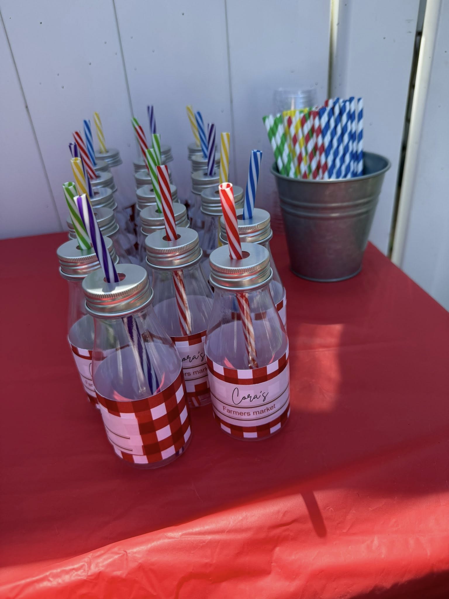 Glass milk bottles with red gingham labels reading Cora's Farmers Market and colorful striped paper straws.