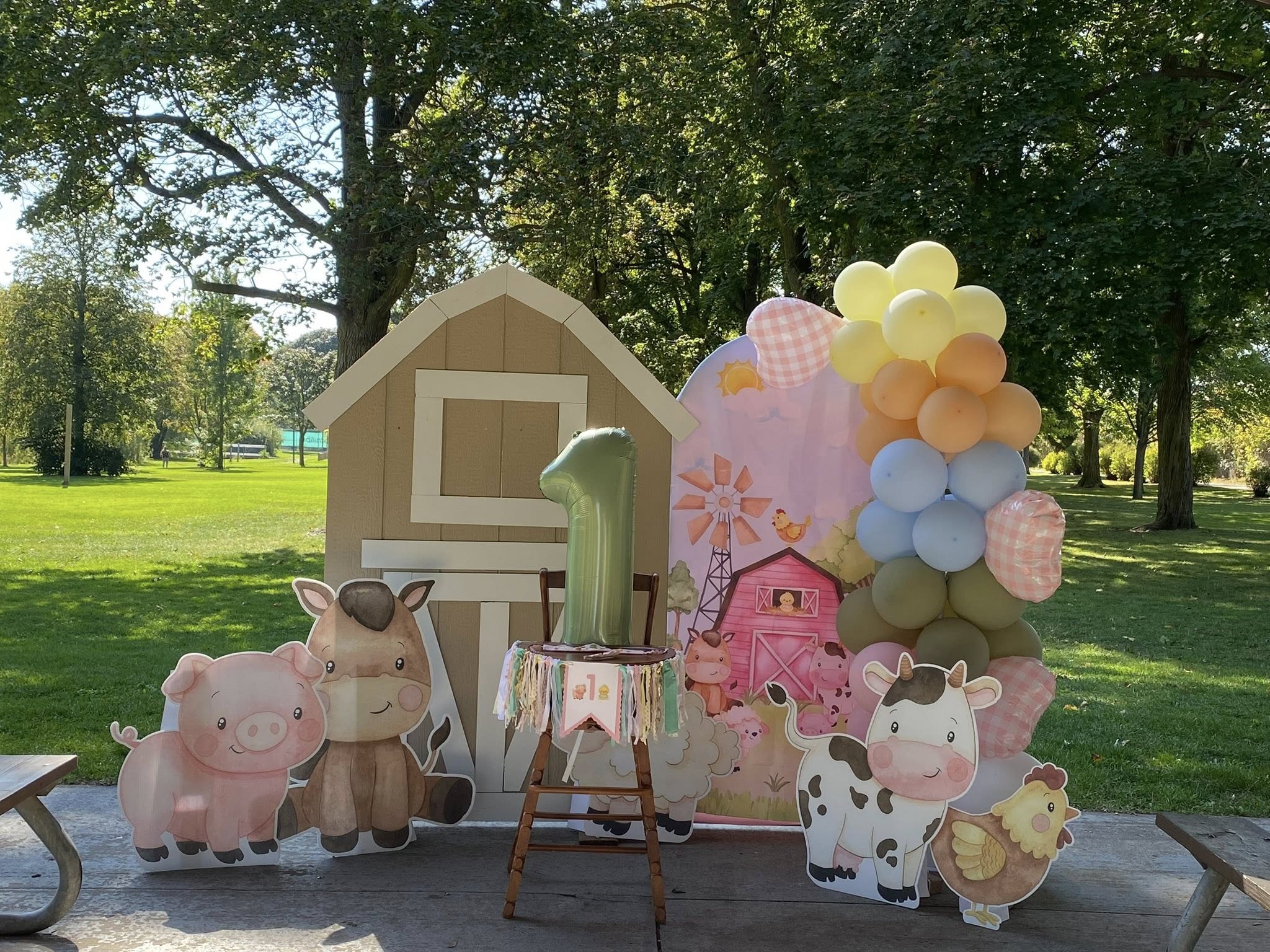 First birthday barnyard theme party decor with cutouts of farm animals and a green number one balloon.