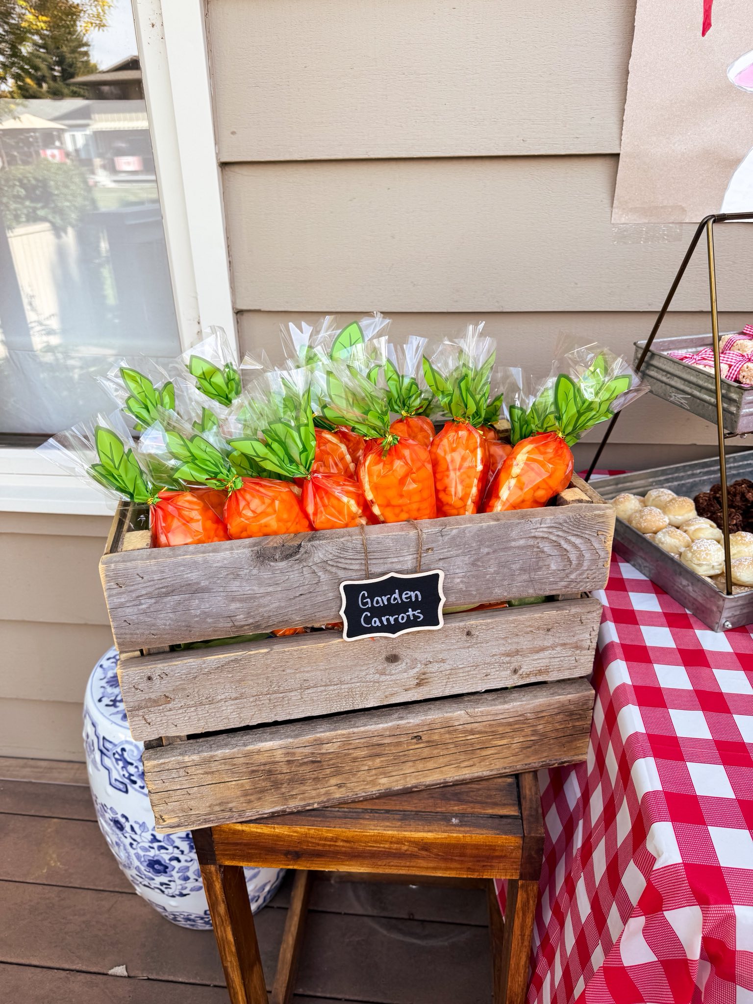 Wooden crate filled with plastic bags of baby carrots shaped like carrots with green paper tops, labeled Garden Carrots