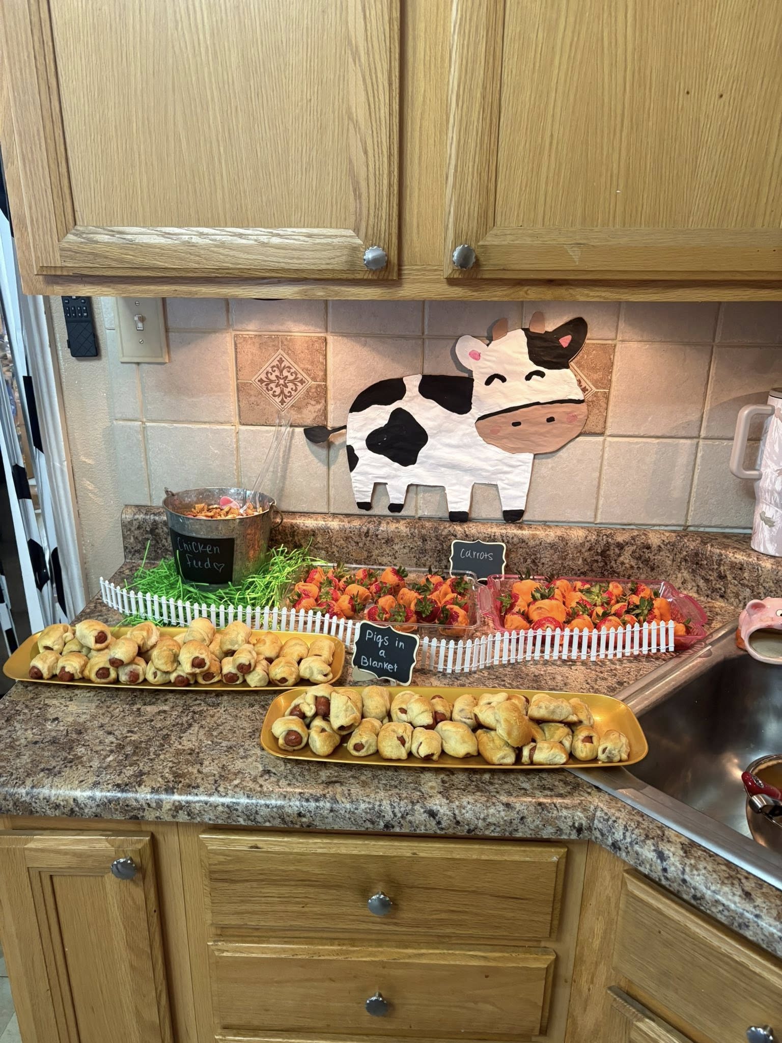 Kitchen counter decorated with a farm theme, featuring platters of pigs in a blanket and carrot-shaped strawberries