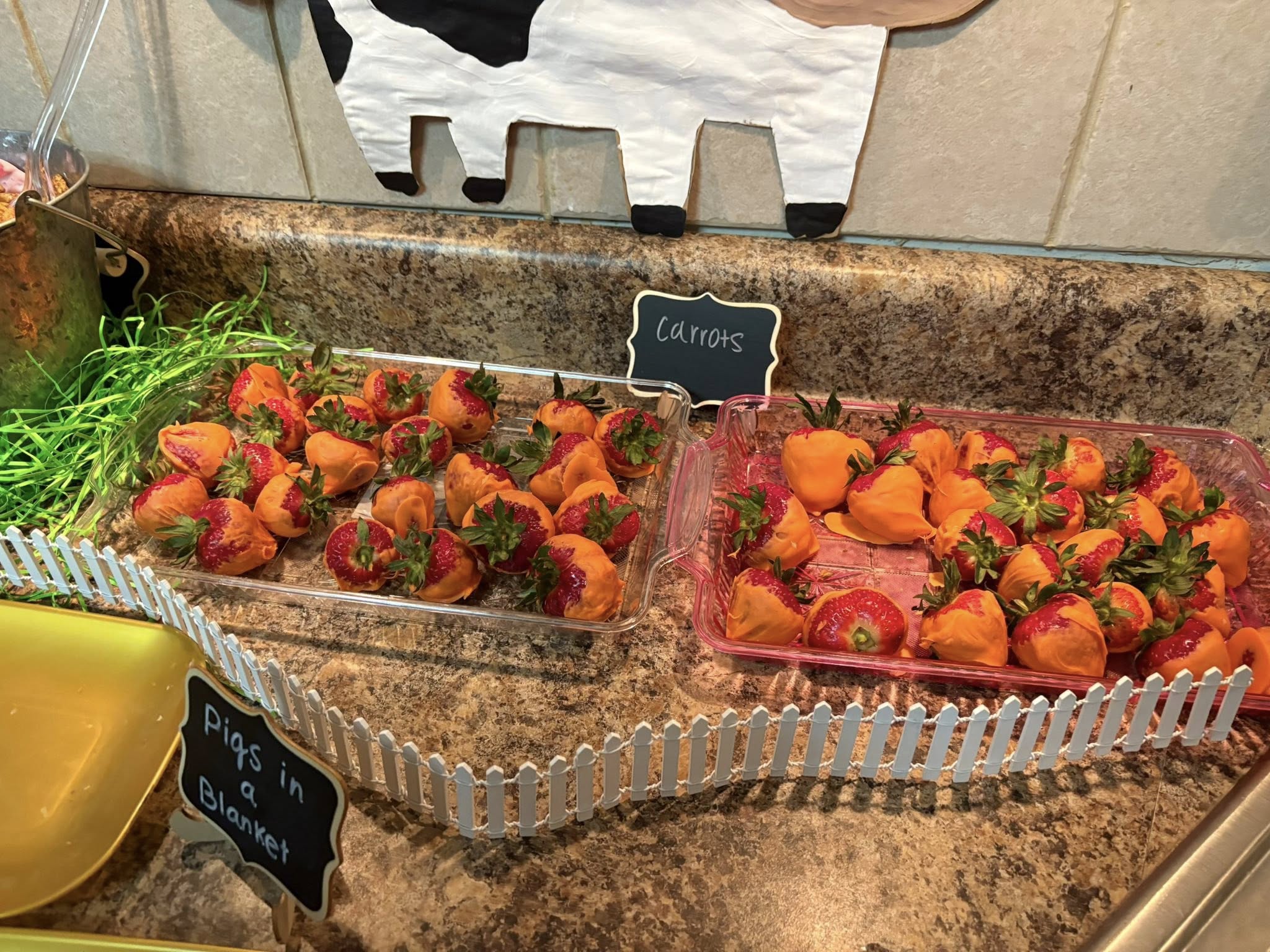 Strawberries dipped in orange candy coating to resemble carrots displayed on a farm-themed party table.