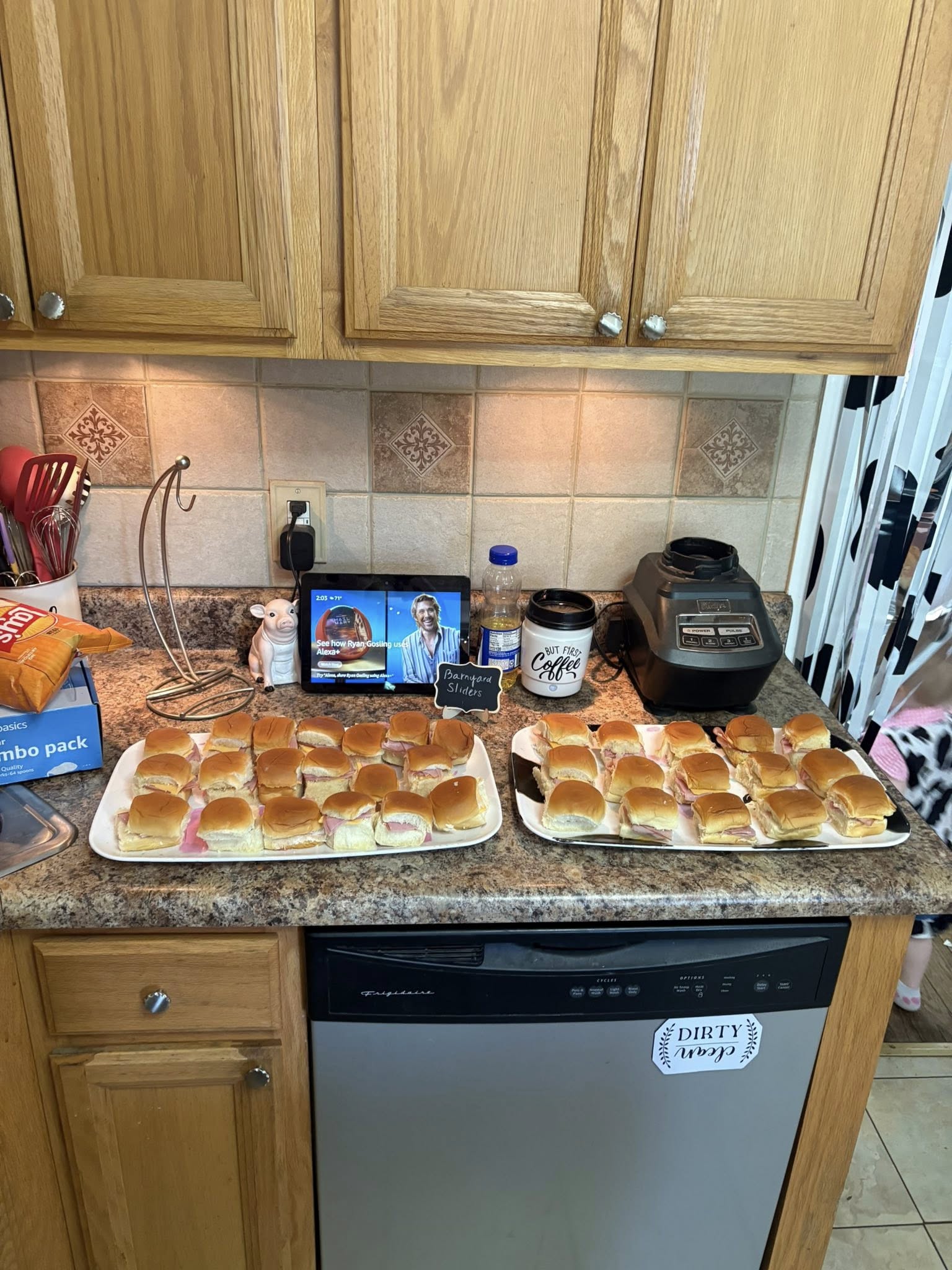Two large platters of ham and cheese sliders served on a kitchen counter for a party.