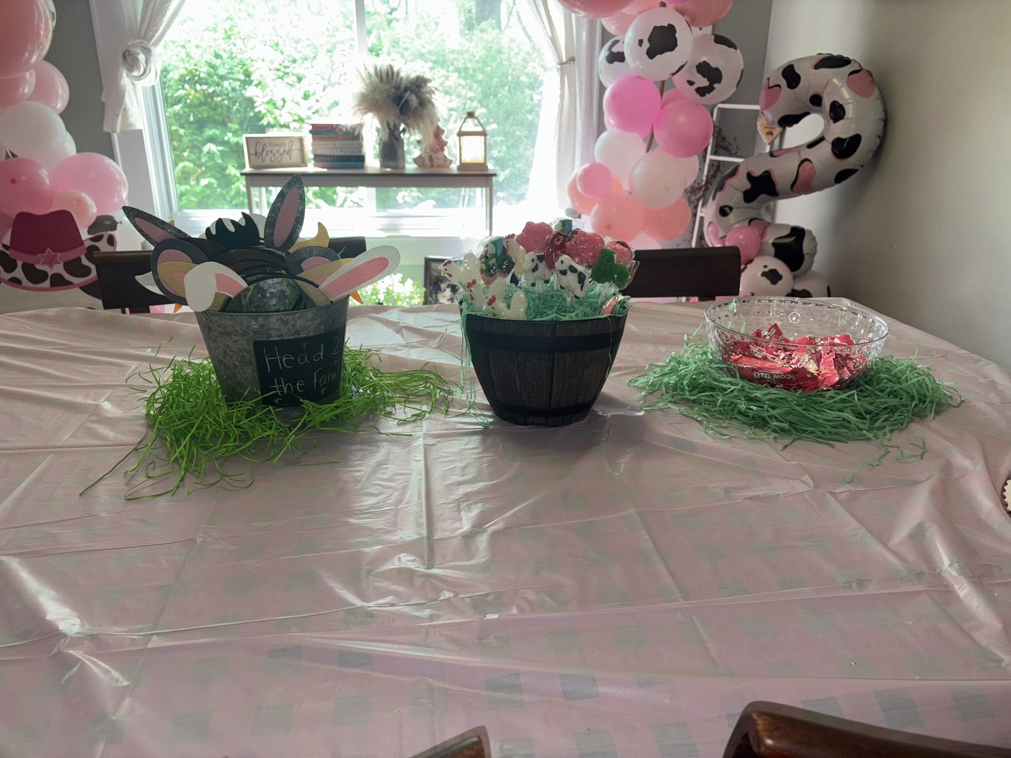 Table decorated for a farm-themed second birthday party featuring cow print balloon decor and baskets of party favors.