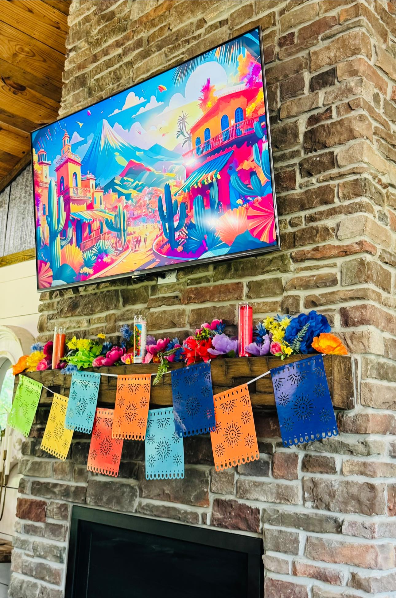 Colorful papel picado banner and artificial flower garland decorating a stone fireplace mantel.