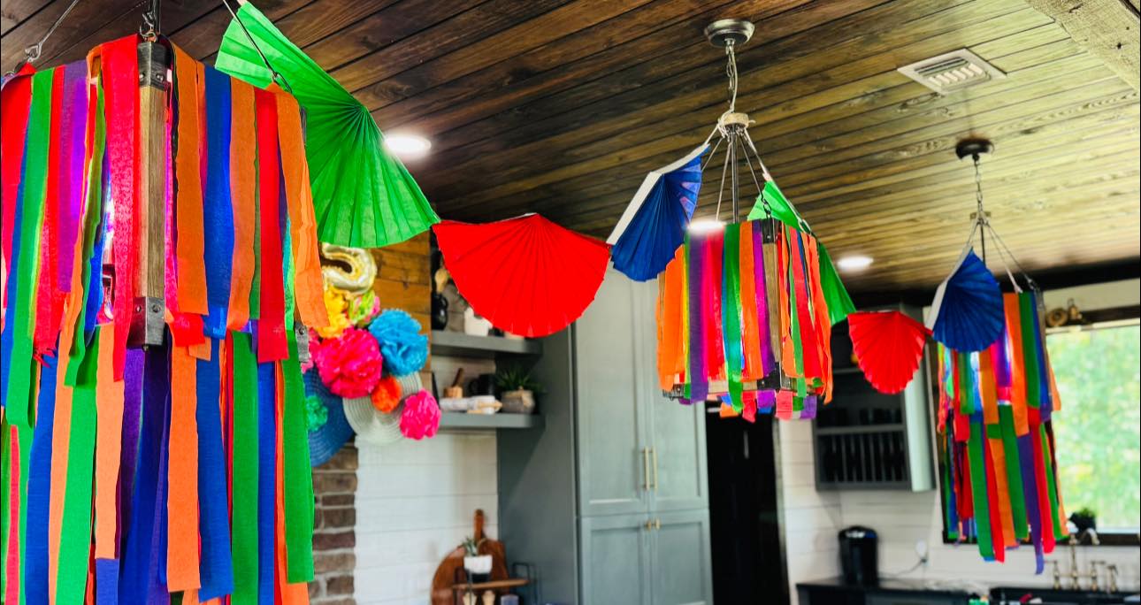 Colorful party streamers and paper fan decorations hanging from ceiling lights.