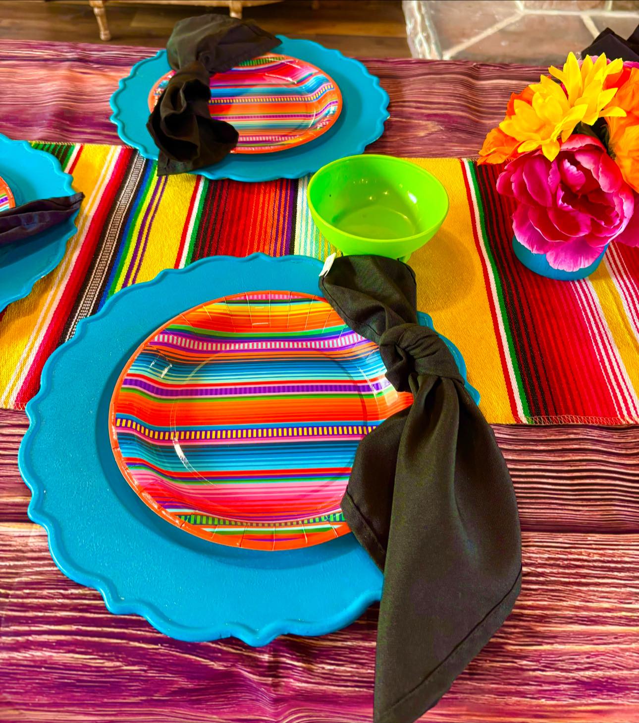 Fiesta-themed table setting with colorful striped plates, teal chargers, and black cloth napkins.