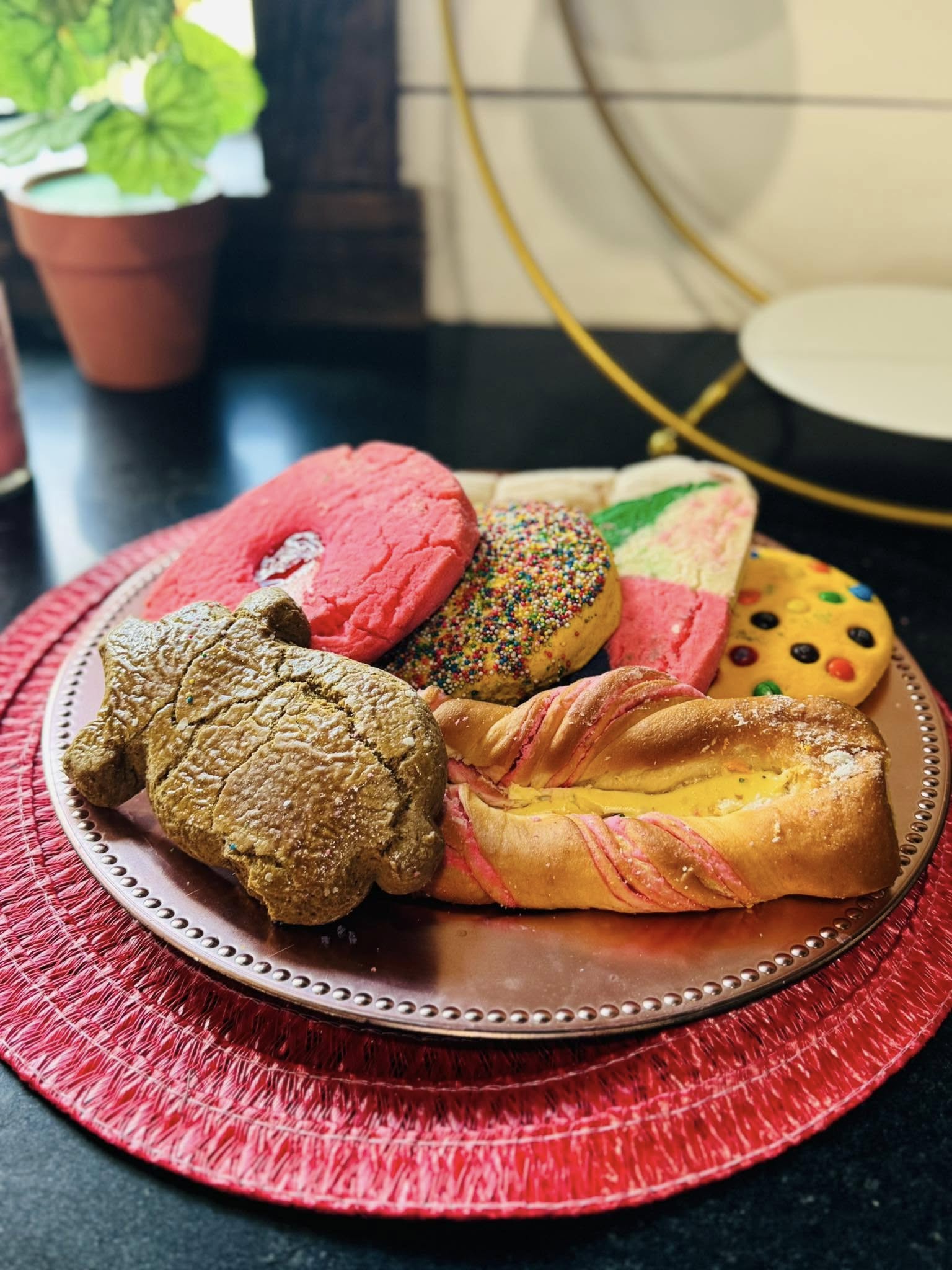 Assorted Mexican sweet breads including a cochinito, sprinkles cookie, and fruit-filled pastry on a copper plate.