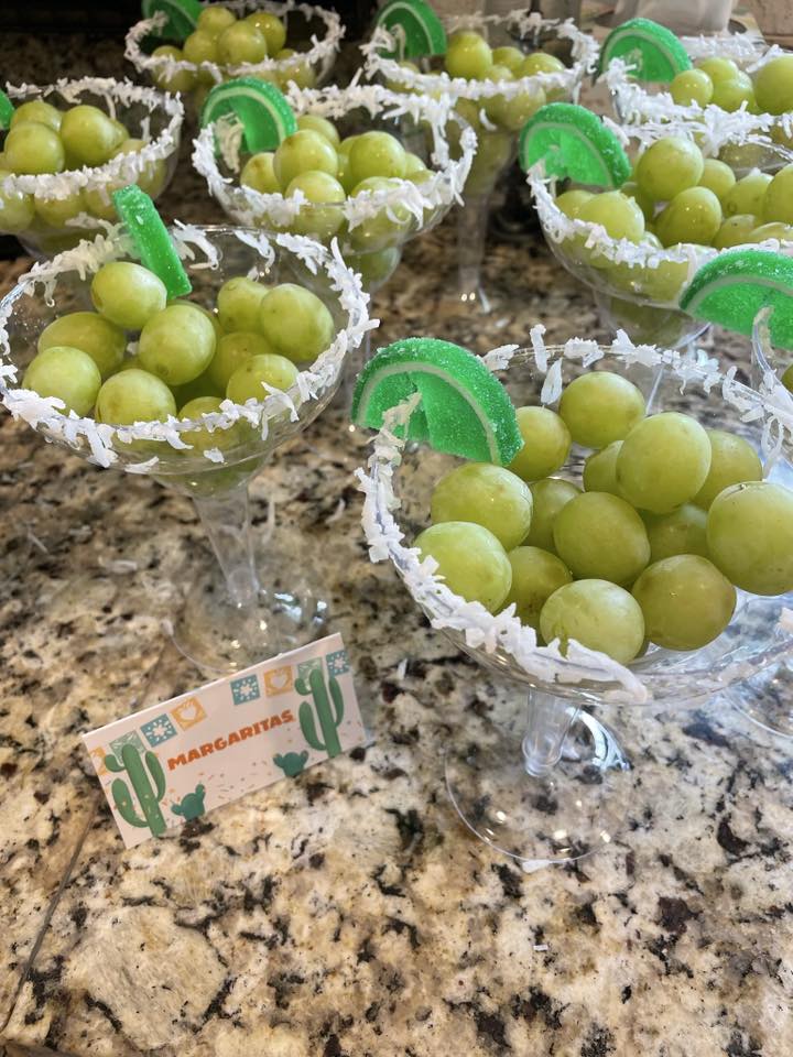Margarita-style glasses filled with green grapes and decorated with shredded coconut rims and gummy lime wedges