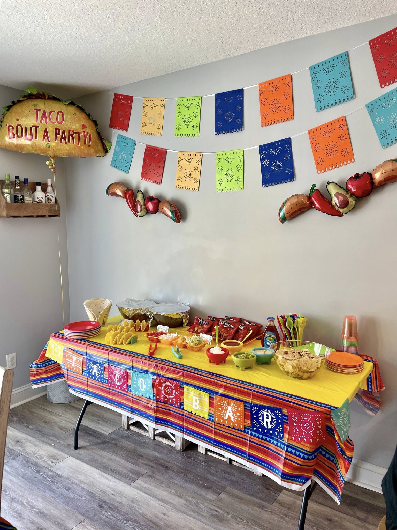 Taco bar party set up with colorful festive decorations, balloons, chips, and toppings.