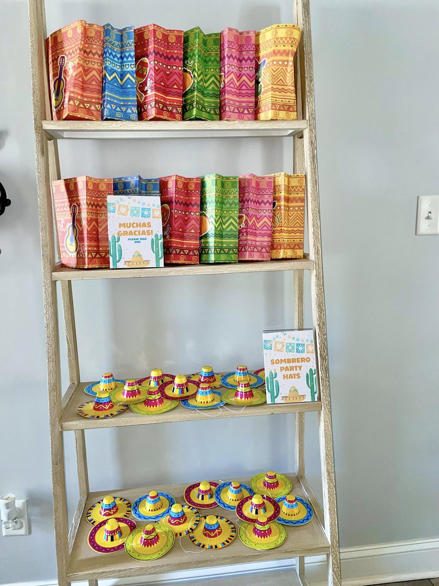 Ladder shelf displaying colorful fiesta treat bags and miniature sombrero party hats with signage.
