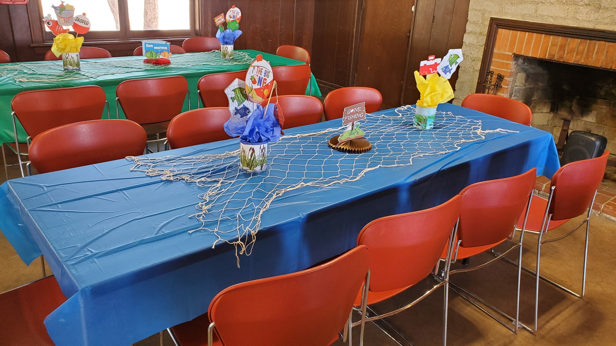 Tables set for a Gone Fishing themed birthday party with blue tablecloths, fishing net runners, and fish centerpieces