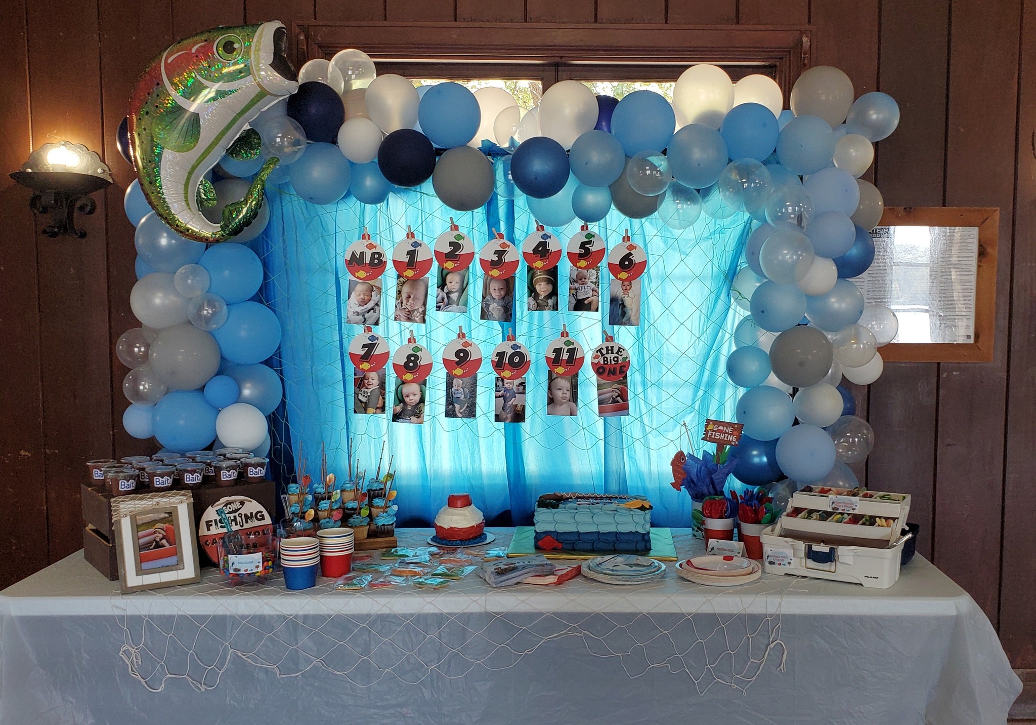 Gone Fishing themed first birthday party decoration setup with a balloon arch and photo milestone display.