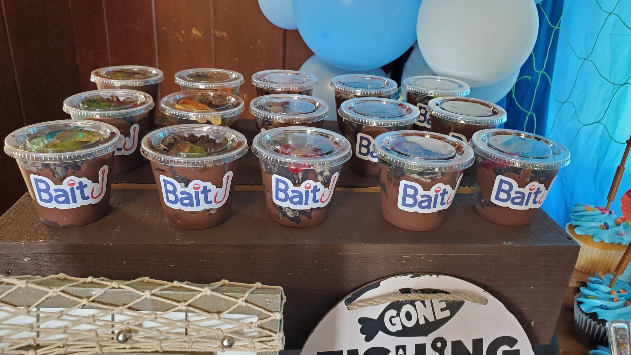 Plastic cups labeled Bait filled with chocolate mousse and gummy worms for a fishing themed party