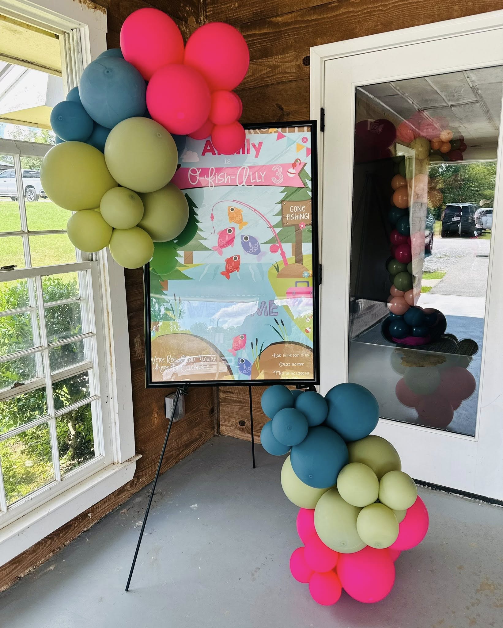 Fishing-themed birthday welcome sign decorated with pink, blue, and lime green balloons.