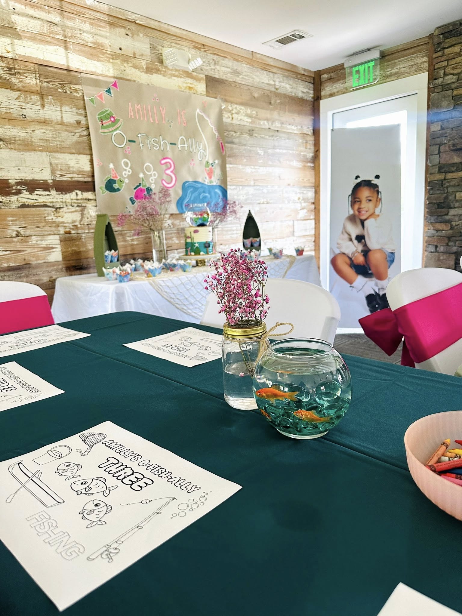 Table decorated for a O-Fish-Ally Three themed birthday party with activity placemats and a goldfish bowl.