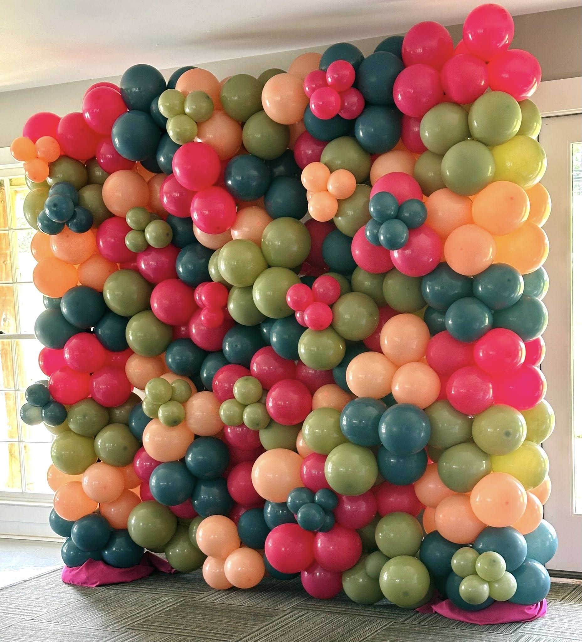 Full wall backdrop made of multicolored balloons in pink, orange, sage green, and dark teal.