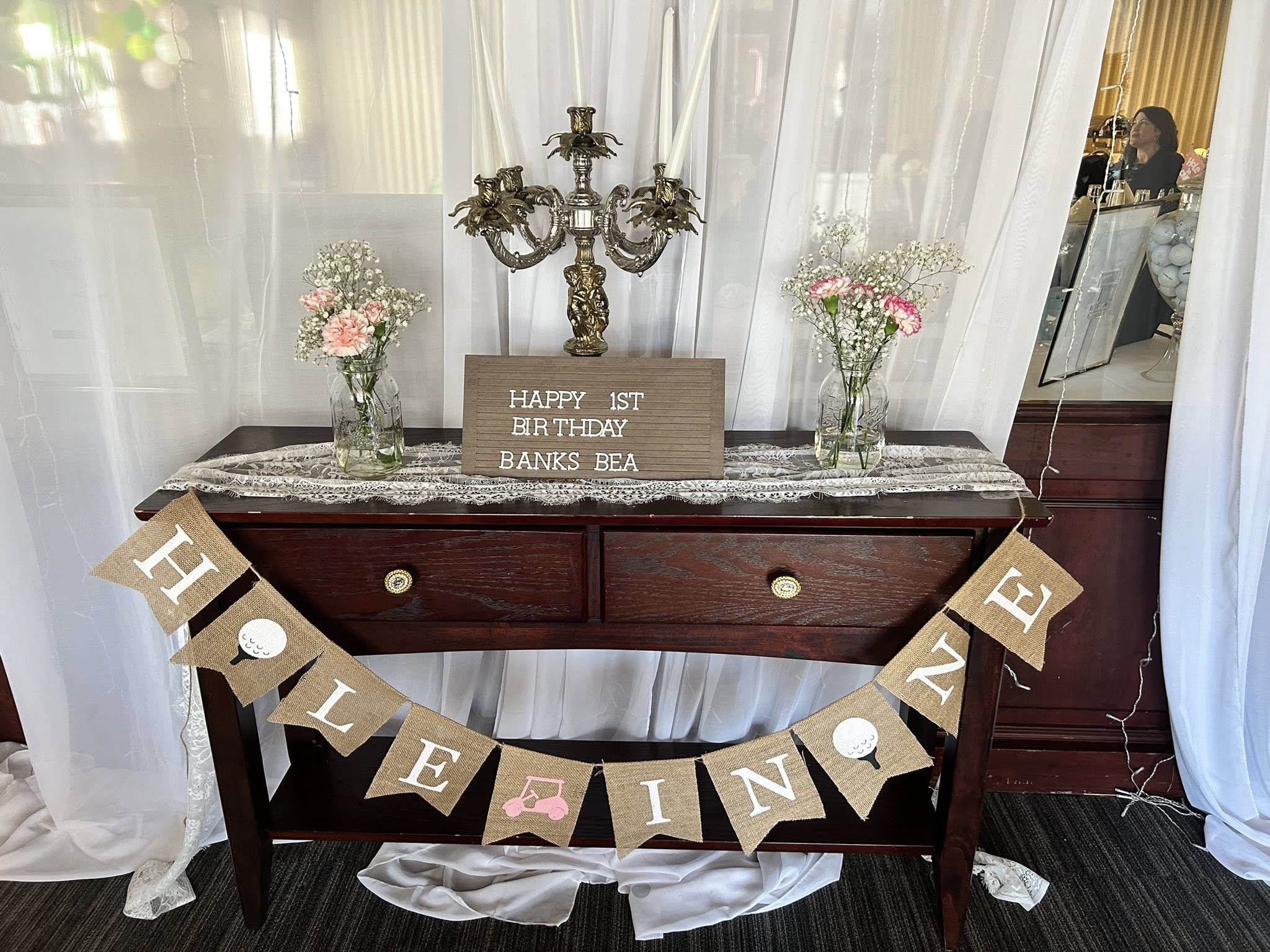 Table decorated for a girl's first birthday party with golf-themed burlap bunting and a letter board sign