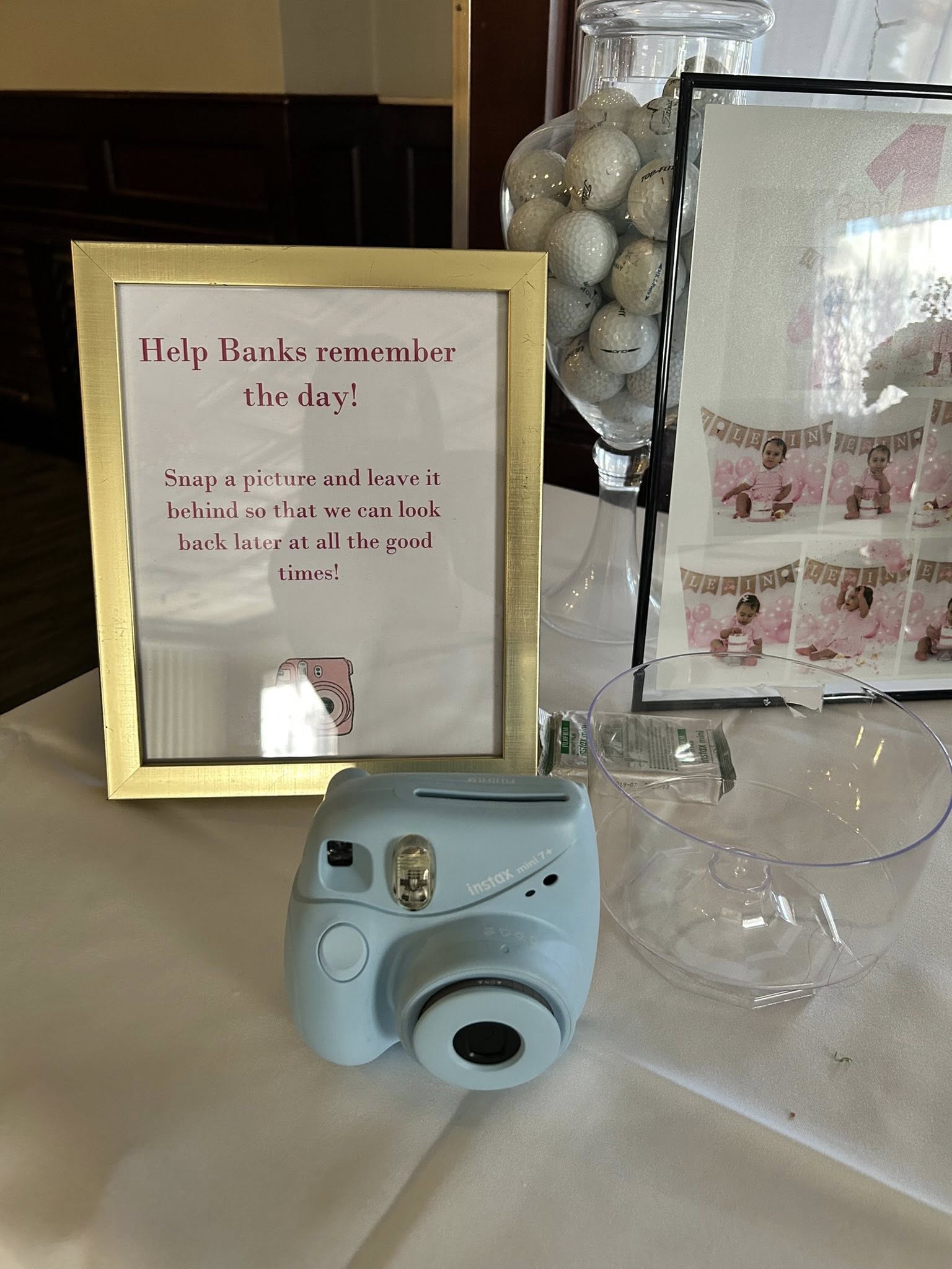 Light blue Instax instant camera on a table with a sign asking guests to leave photos for the party.