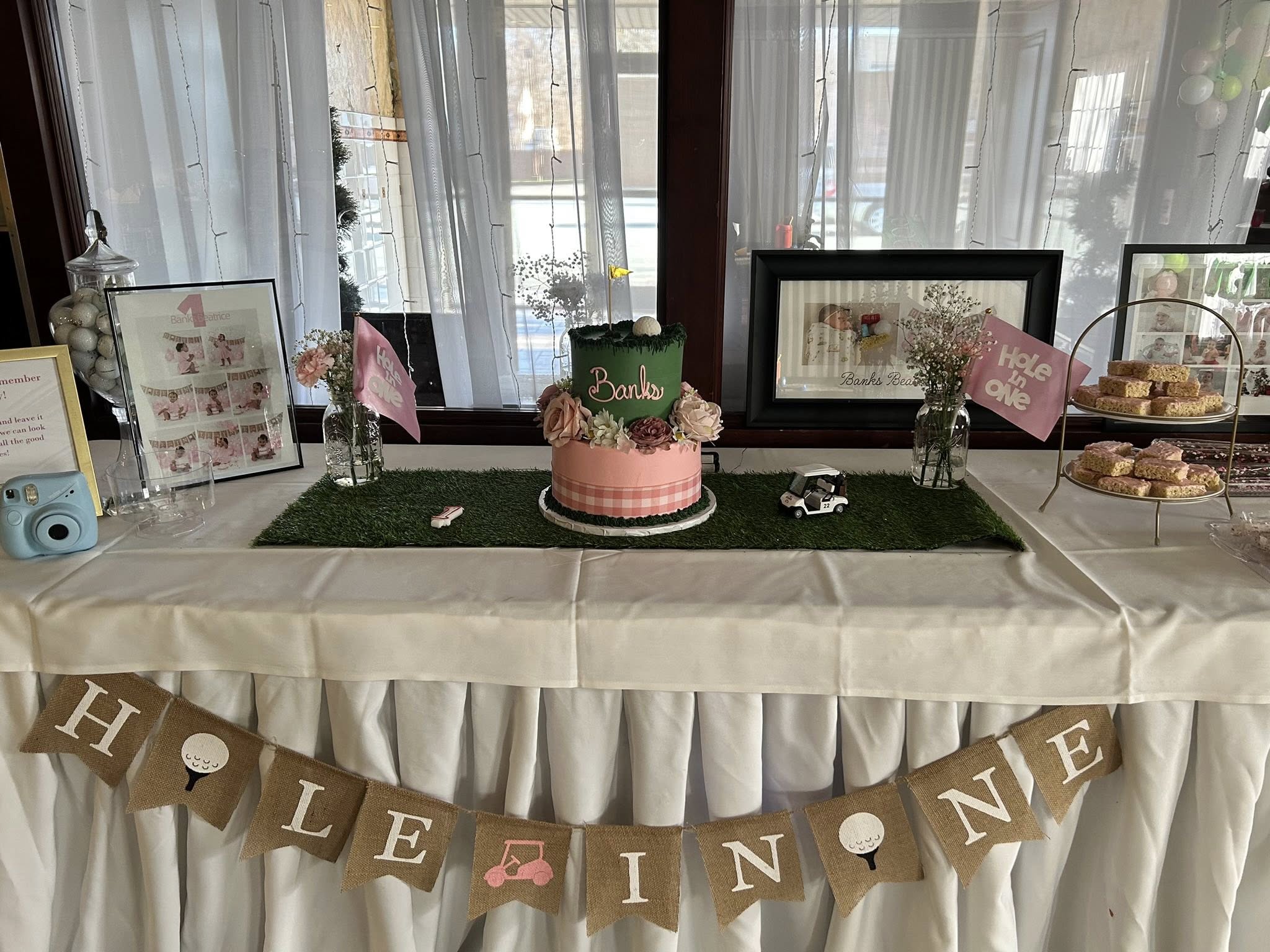 Table decorated for a girl's first birthday golf-themed party with a tiered cake and Hole in One banner.