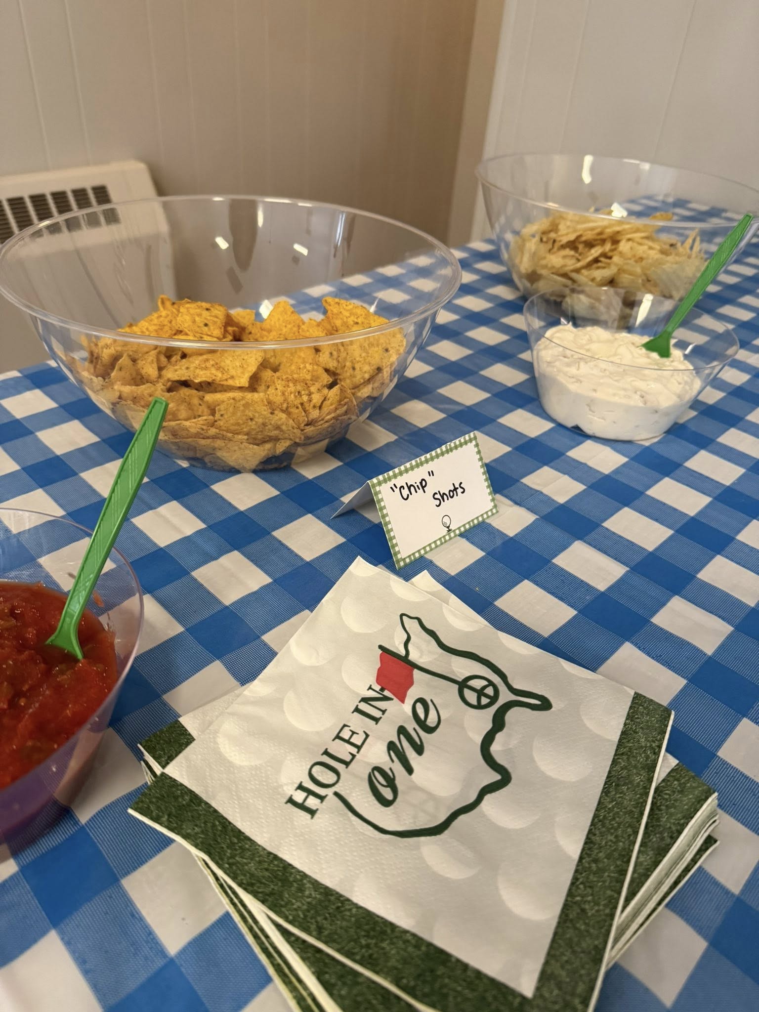 Snack table with bowls of chips, dip, and salsa, and napkins printed with a golf-themed Hole In One design.