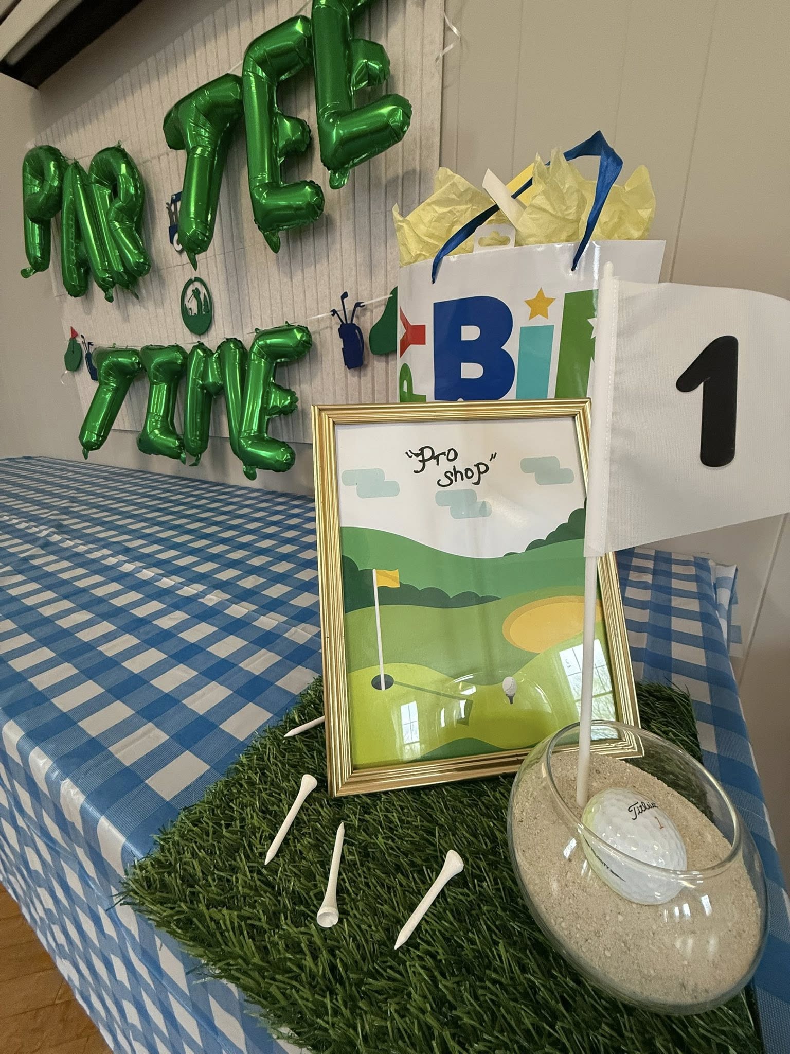 Golf-themed birthday party table decor featuring a Par-Tee Time sign, a framed Pro Shop illustration, and hole 1 flag