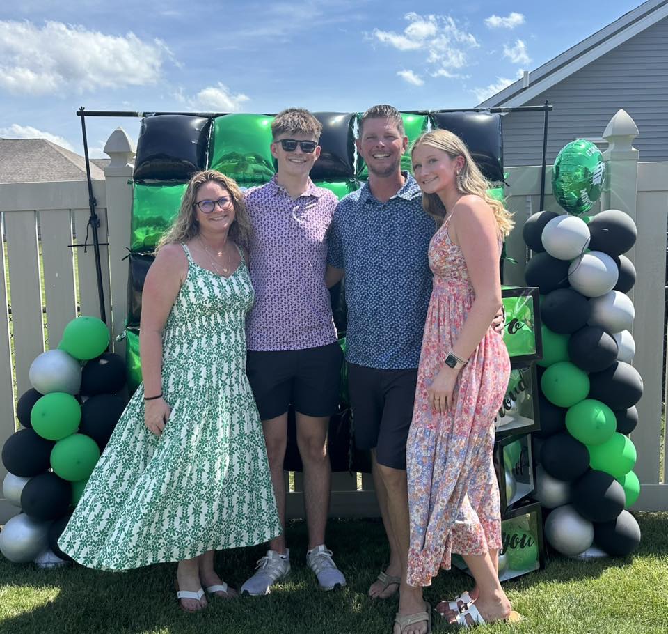 Family standing in front of a green and black balloon backdrop at a graduation party.