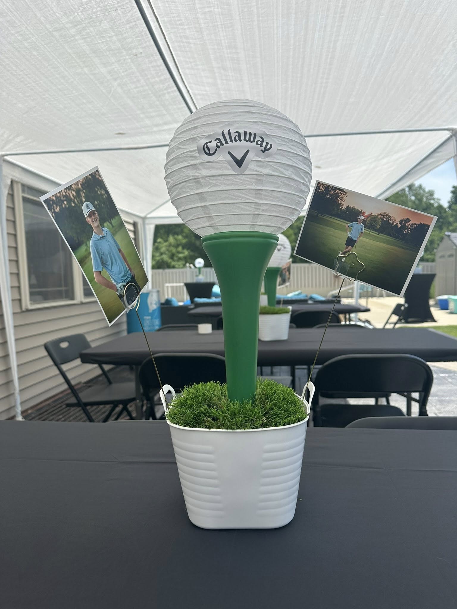 Golf-themed table centerpiece featuring a Callaway golf ball lantern on a tee in a pot with photos of a golfer.