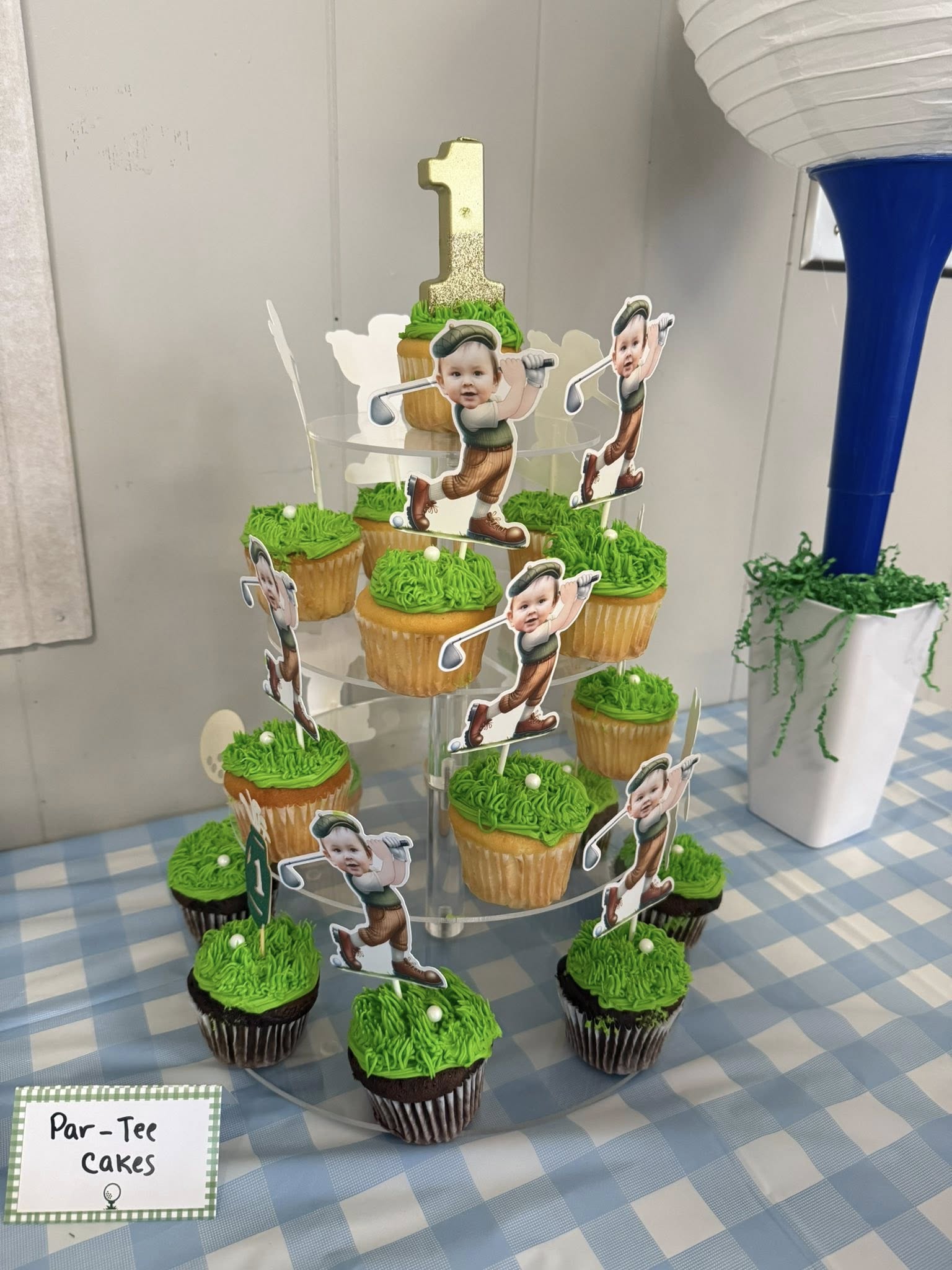 Cupcake stand featuring grass-frosted cupcakes with customized golfer toppers and a gold number one cake topper.