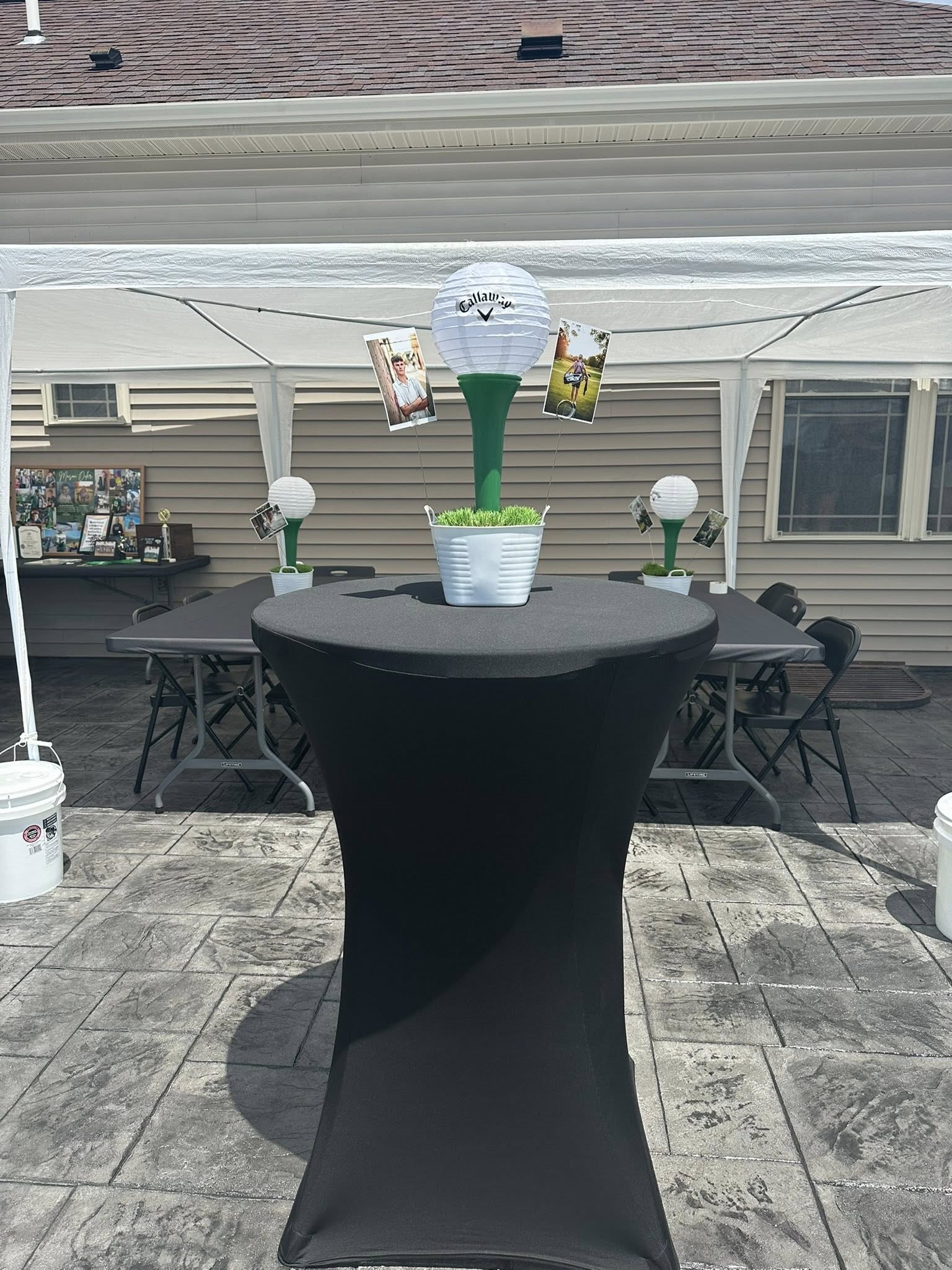 Golf-themed table centerpiece with a paper golf ball decoration, faux grass, and attached photos of a golfer.