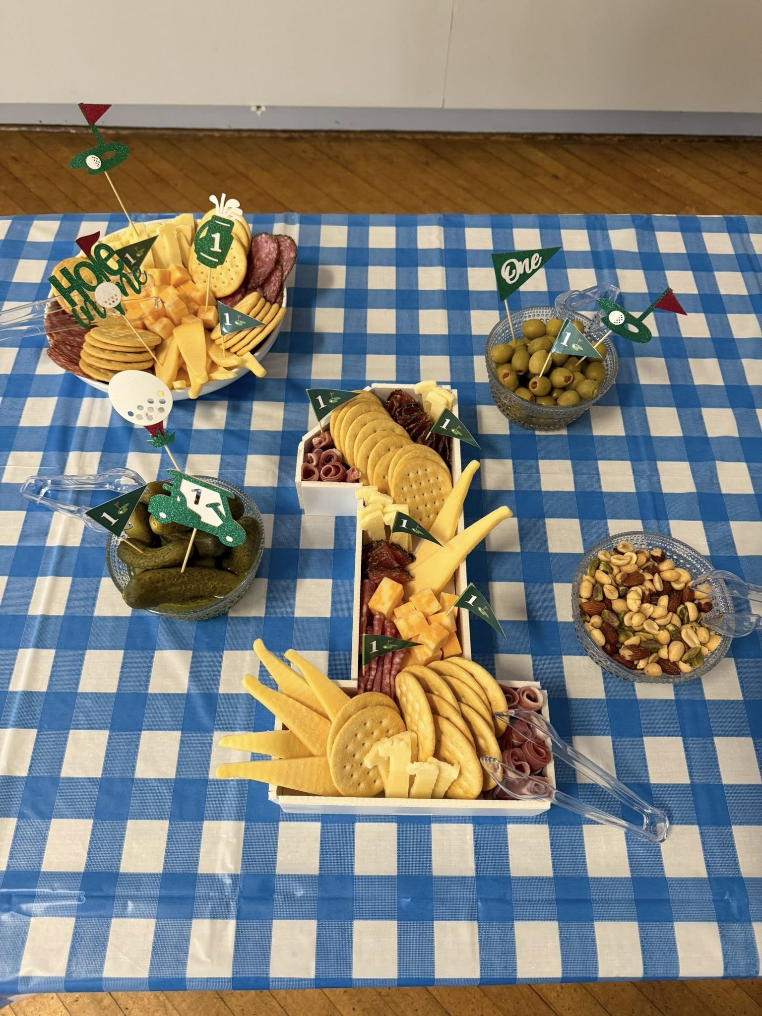 Golf-themed first birthday party food spread featuring a number one shaped wooden charcuterie board and snacks.