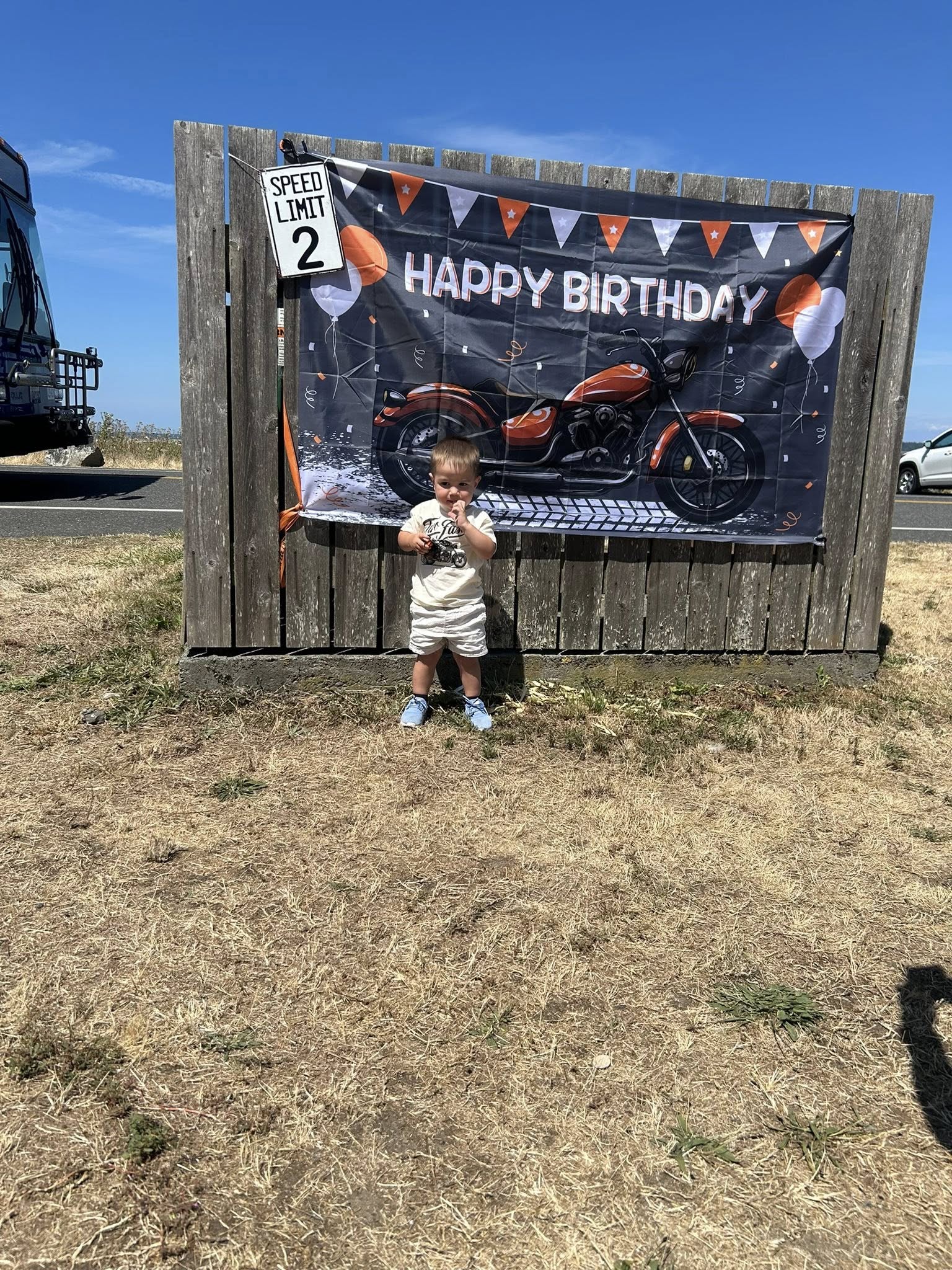 Toddler wearing a motorcycle t-shirt standing in front of a motorcycle-themed second birthday backdrop